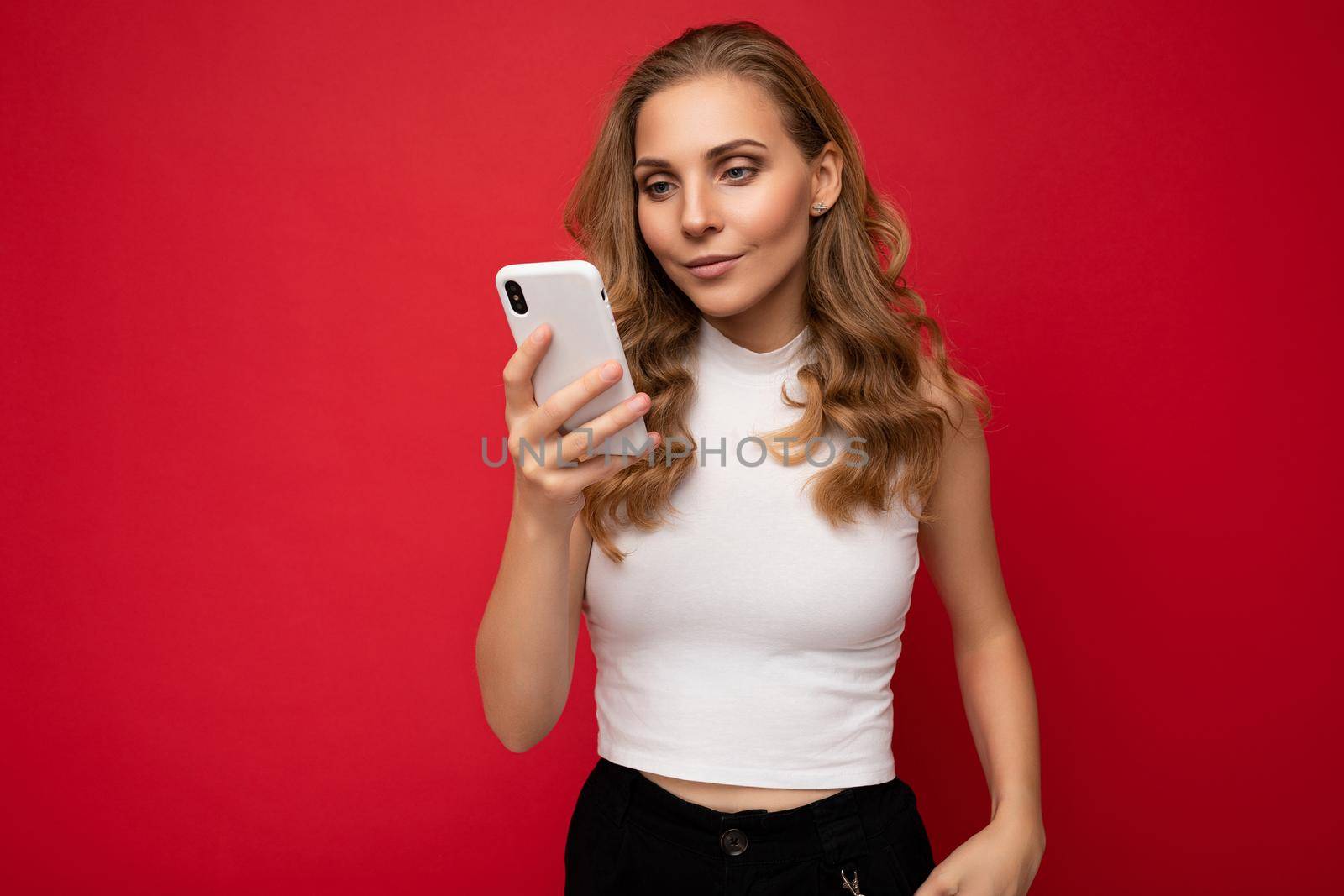 Beautiful young woman wearing casual clothes standing isolated over background surfing on the internet via phone looking at mobile screen.