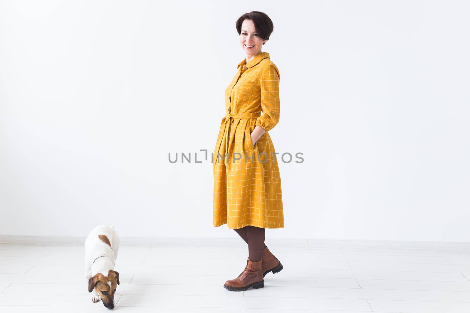 Cheerful young woman posing in a yellow dress with her beloved dog Jack Russell Terrier standing on a white background. The concept of casual wear and pets by Satura86