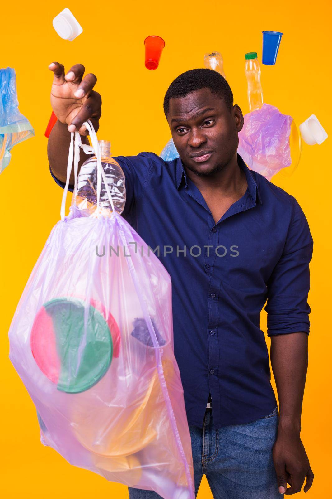 Problem of trash, plastic recycling, pollution and environmental concept - confused man carrying garbage bag on yellow background.