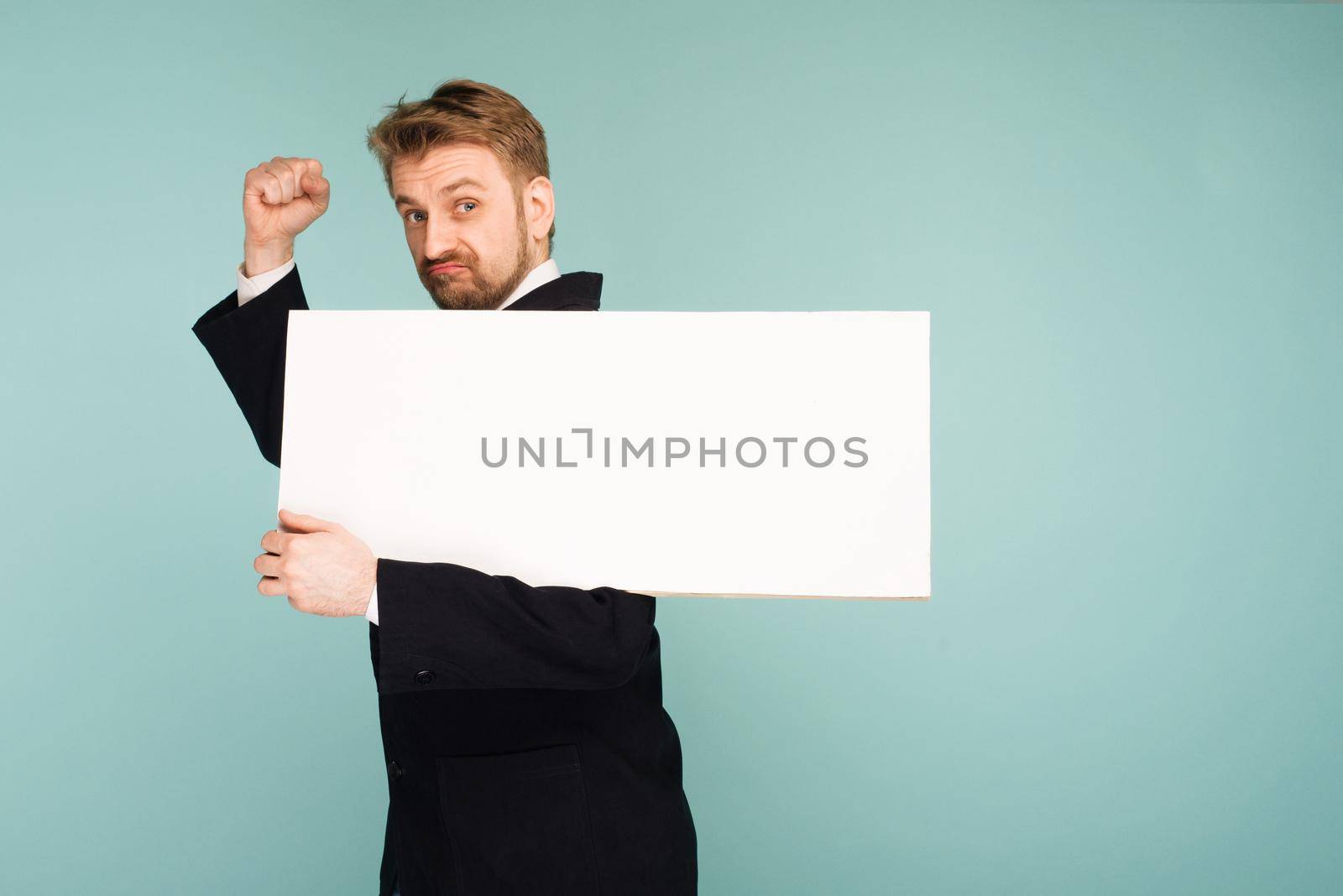 Funny young business man showing blank signboard, on blue background