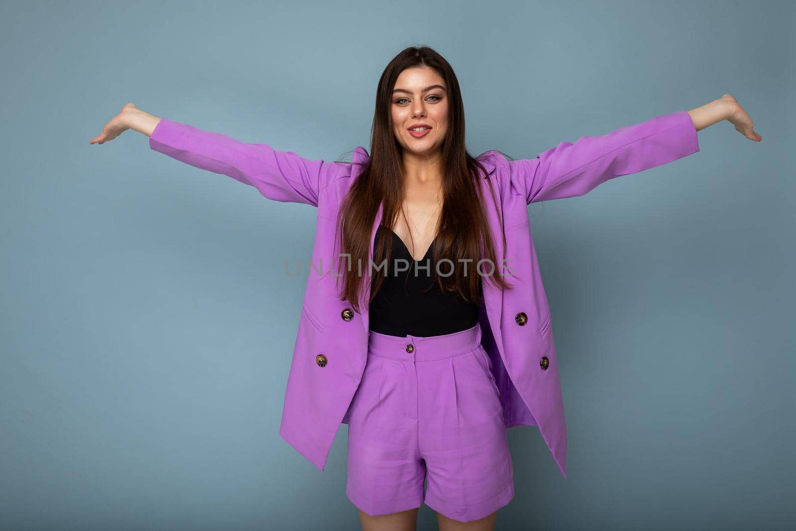 Portrait of happy joyful positive beautiful fashionable brunette woman in casual trendy violet jacket isolated on blue background with free space.