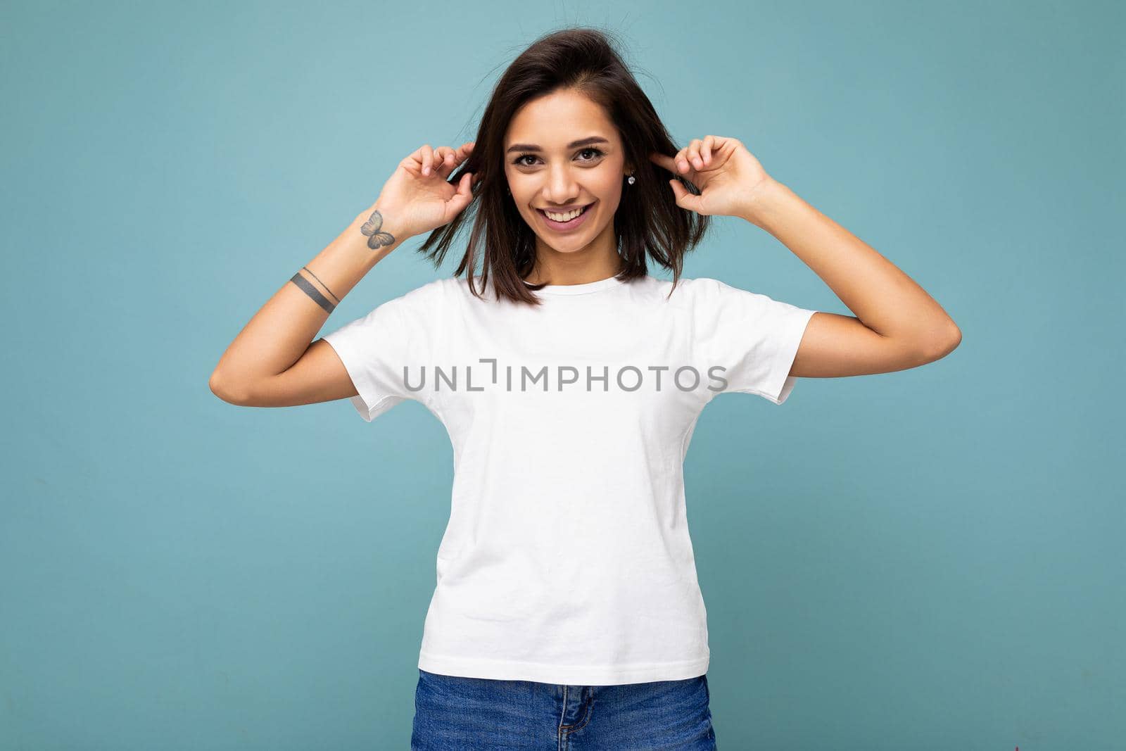Portrait of positive young beautiful brunette woman with sincere emotions wearing casual white t-shirt for mockup isolated over blue background with copy space.