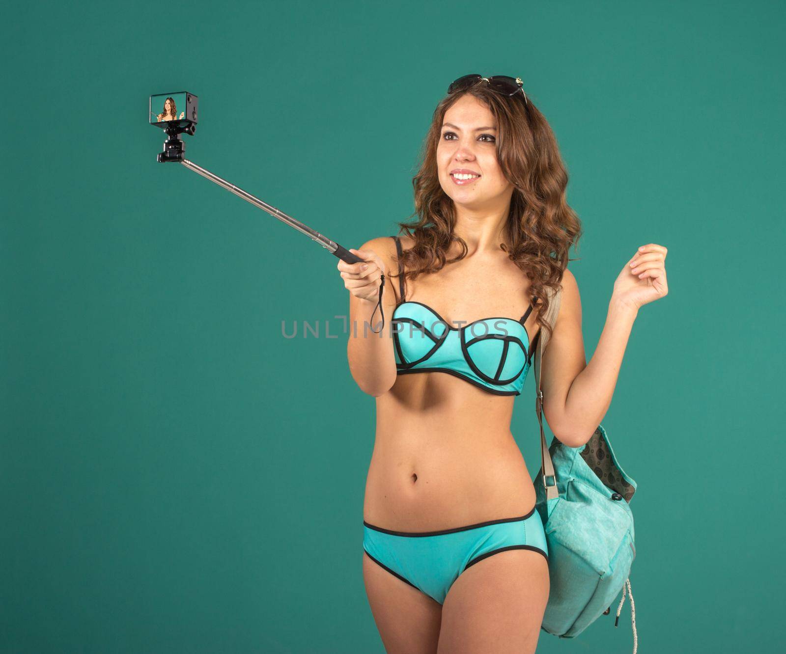 Hipster girl making selfie with action camera on green background wearing swimwear.