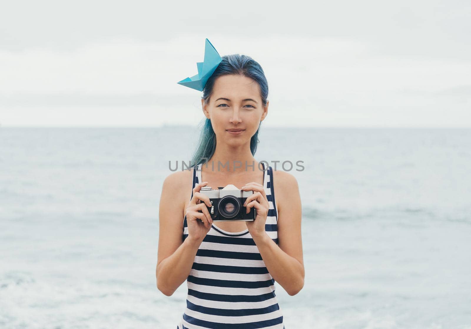 Beautiful young woman with old photo camera standing on background of sea in summer
