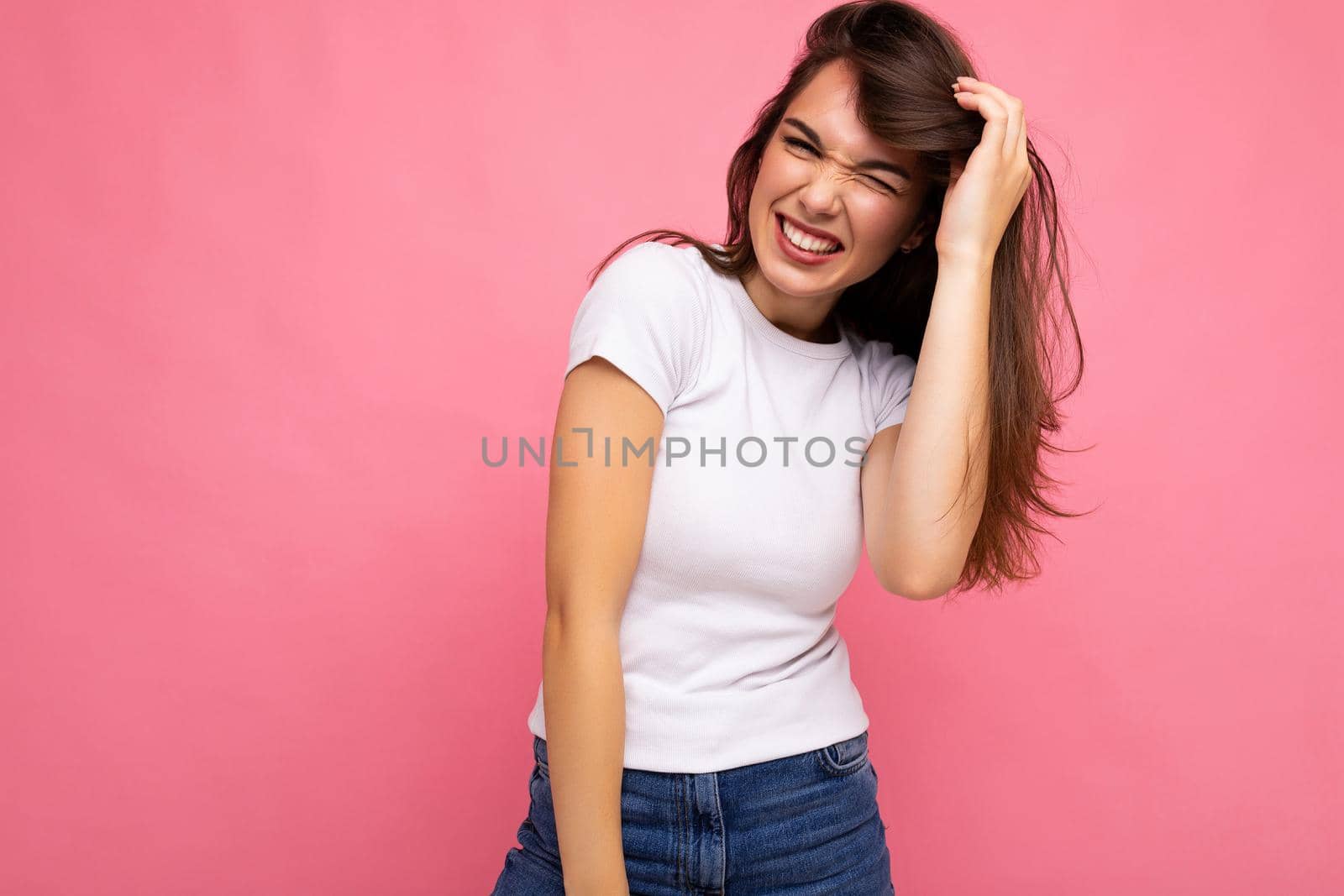 Photo portrait of young beautiful smiling hipster brunette woman in white t-shirt with mockup. Sexy carefree female person posing isolated near pink wall with empty space in studio. Positive model with natural makeup by TRMK