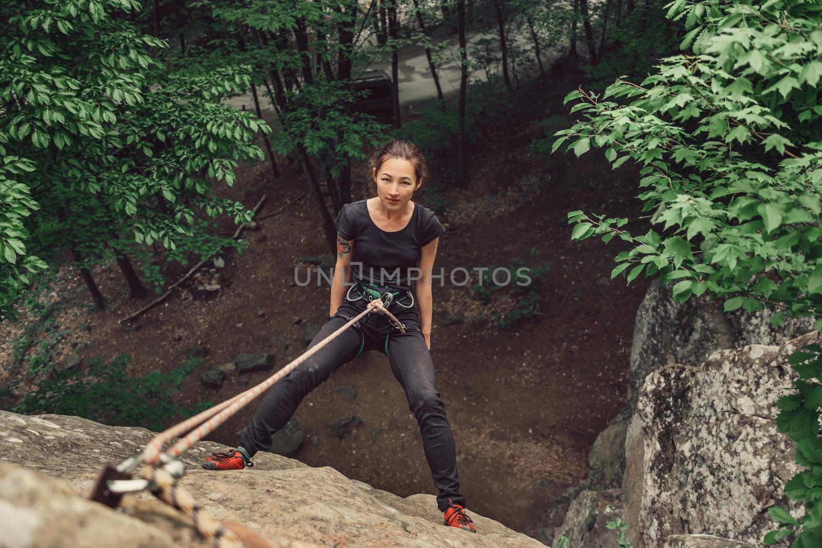 Climber young woman wearing in safety equipment standing on stone rock in summer outdoor, top view