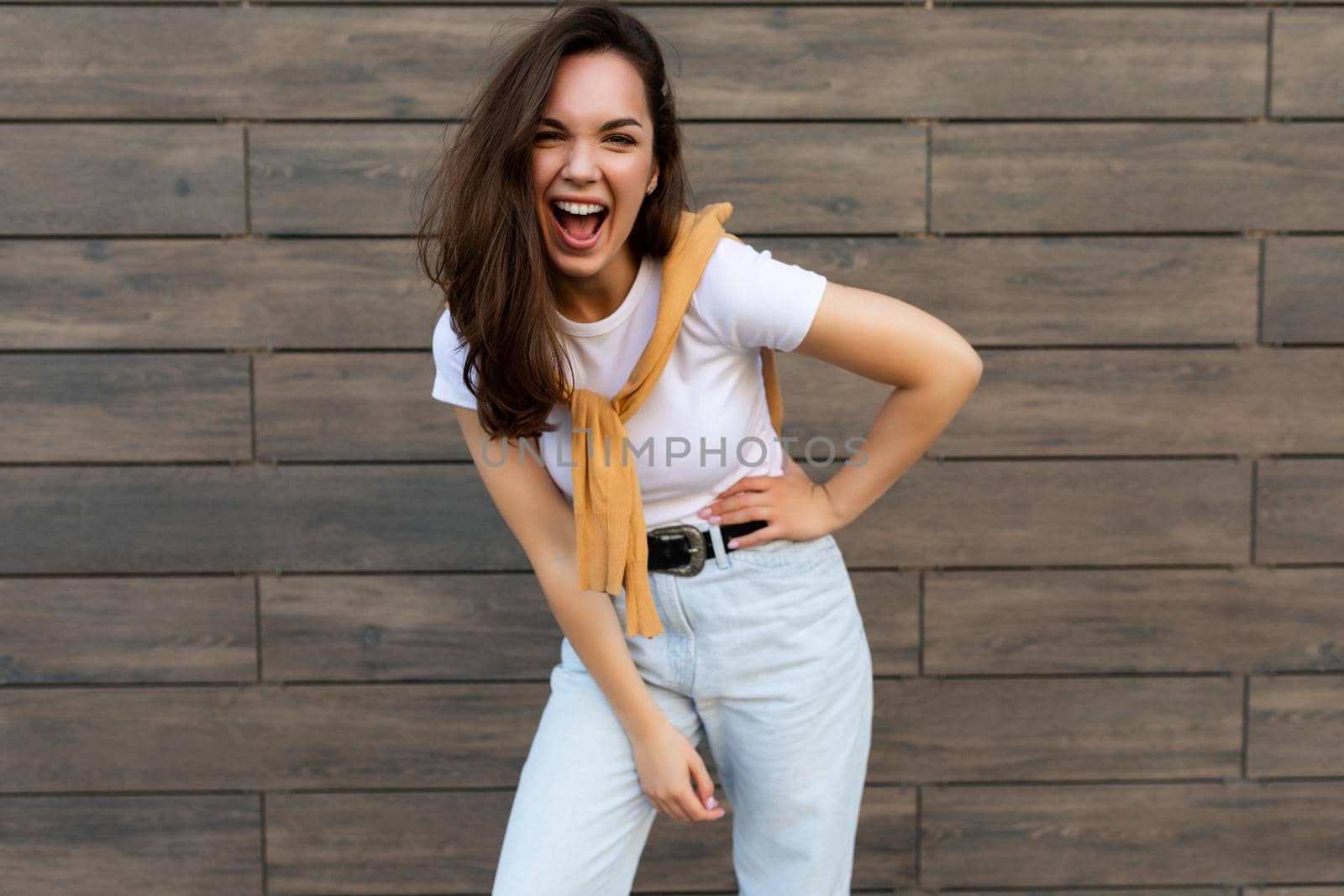 Photo of emotional positive happy joyful pretty young brunette woman in trendy outfit. Beautiful attractive female person standing outside in the street and showing sincere emotions by TRMK