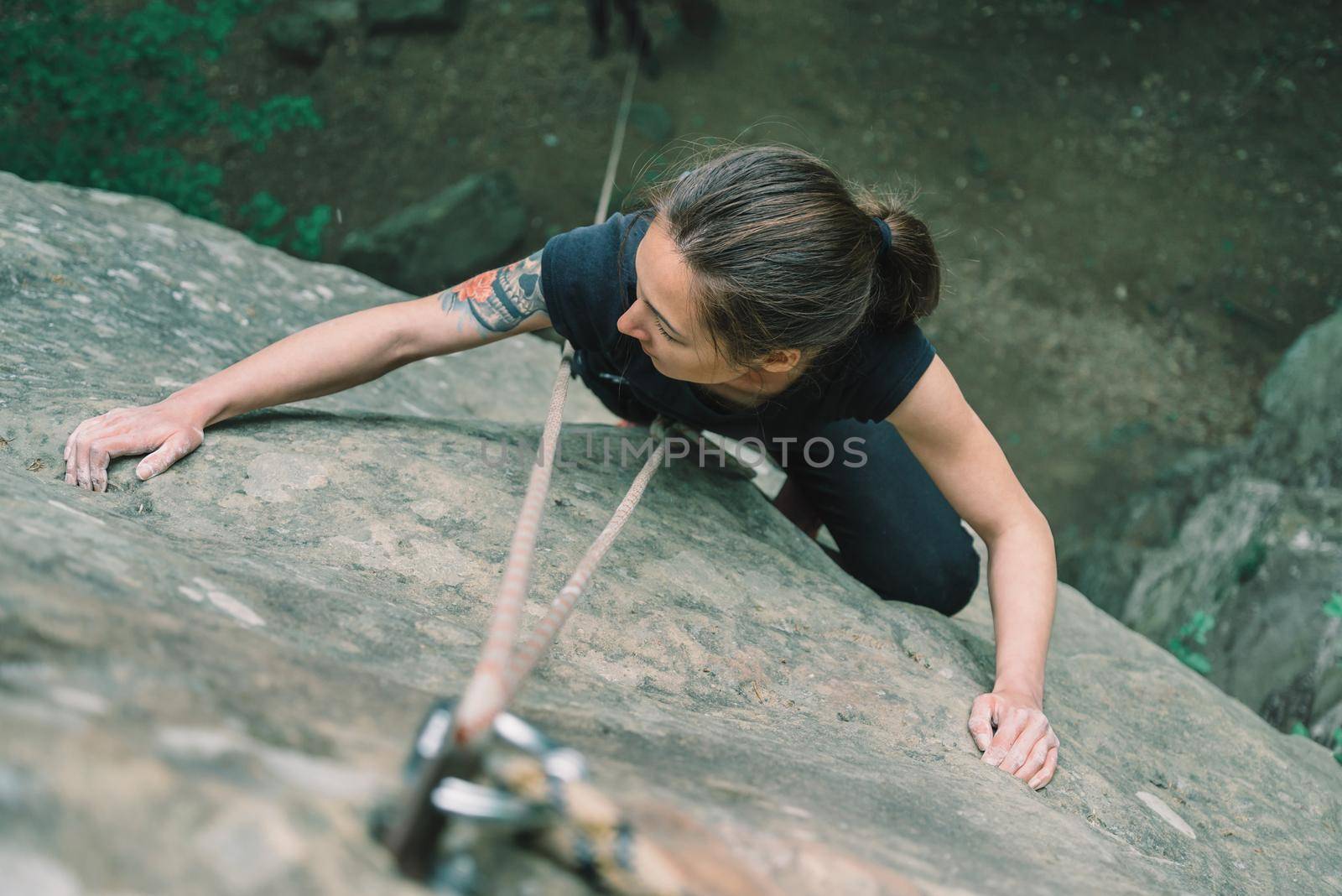 Climber young woman wearing in safety equipment climbing on stone rock in summer outdoor, top view