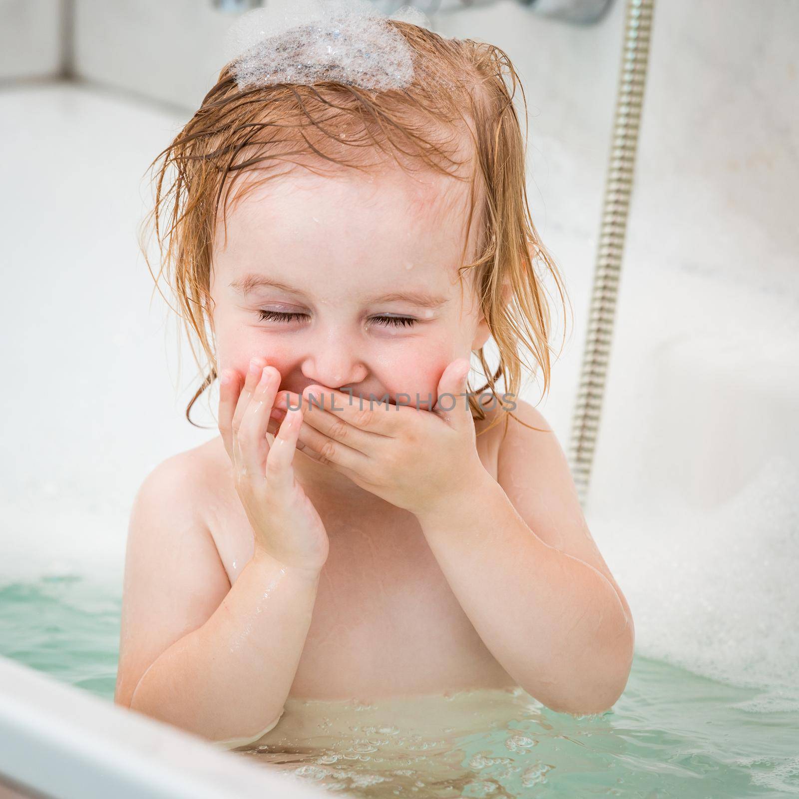 cute two year old baby bathes in a bath with foam closeup