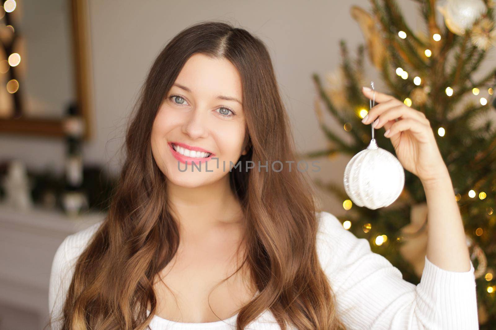 Decorating Christmas tree and winter holidays concept. Happy smiling woman holding festive ornament at home.