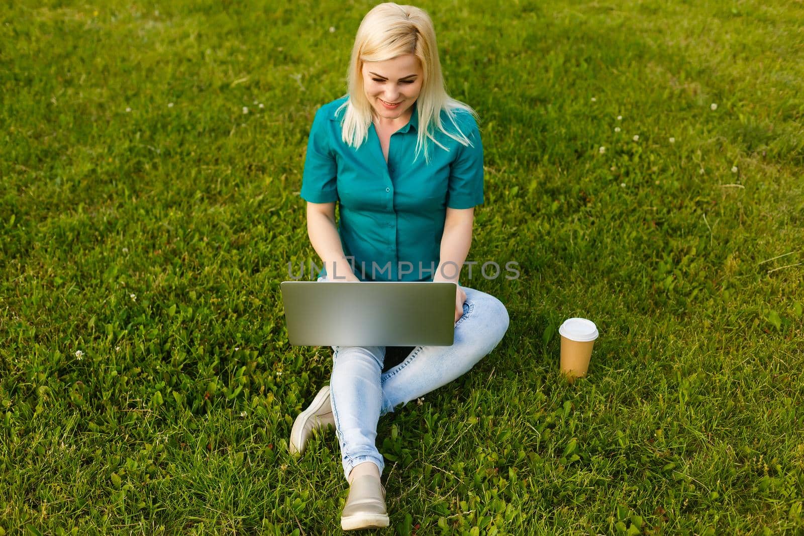 beautiful young blond woman with a laptop in the park on a warm summer day