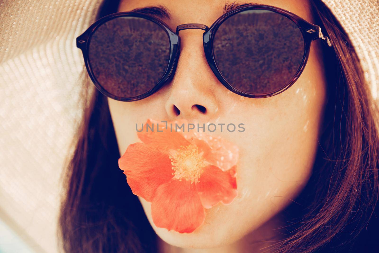 Portrait of attractive girl in sunglasses with red flower, concept of summer mood. Fashionable and beautiful summer girl. Image with instagram color effect