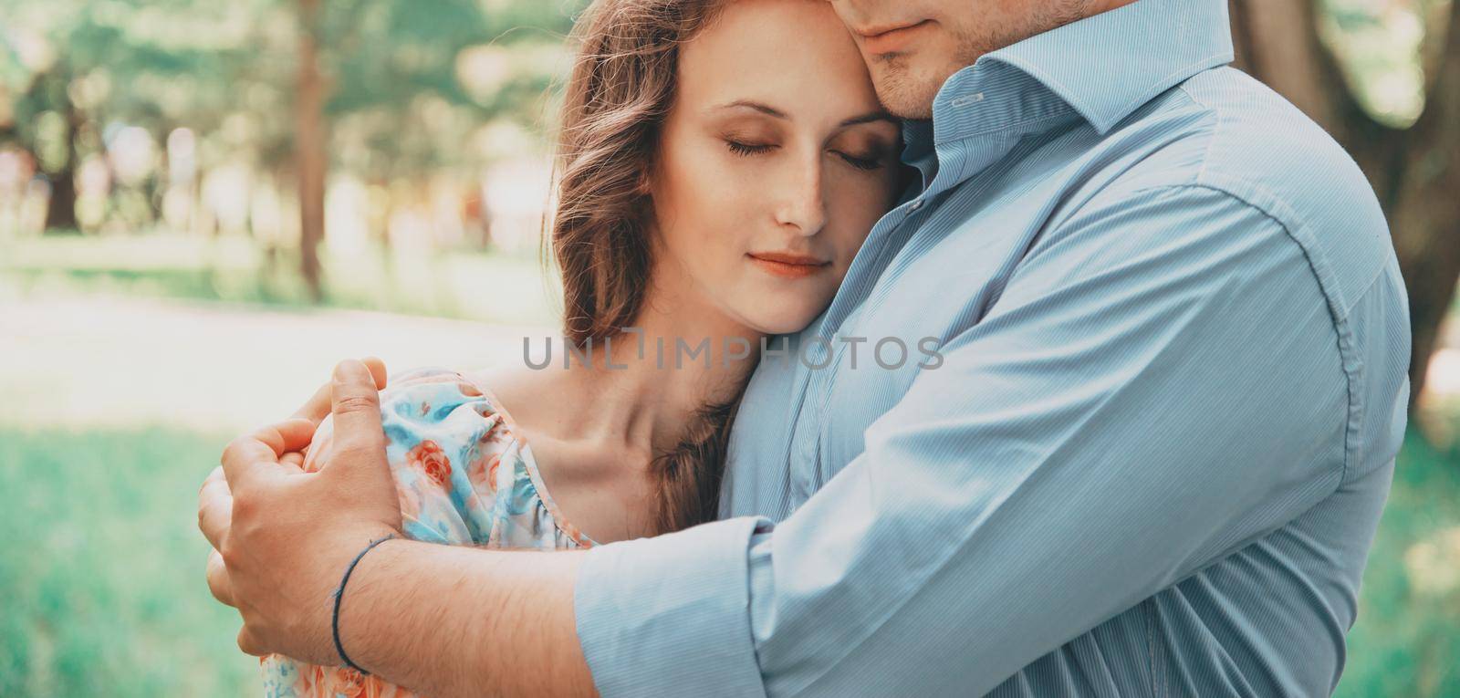 Young couple in love resting in summer park. Man embracing woman with closed eyes, tender scene