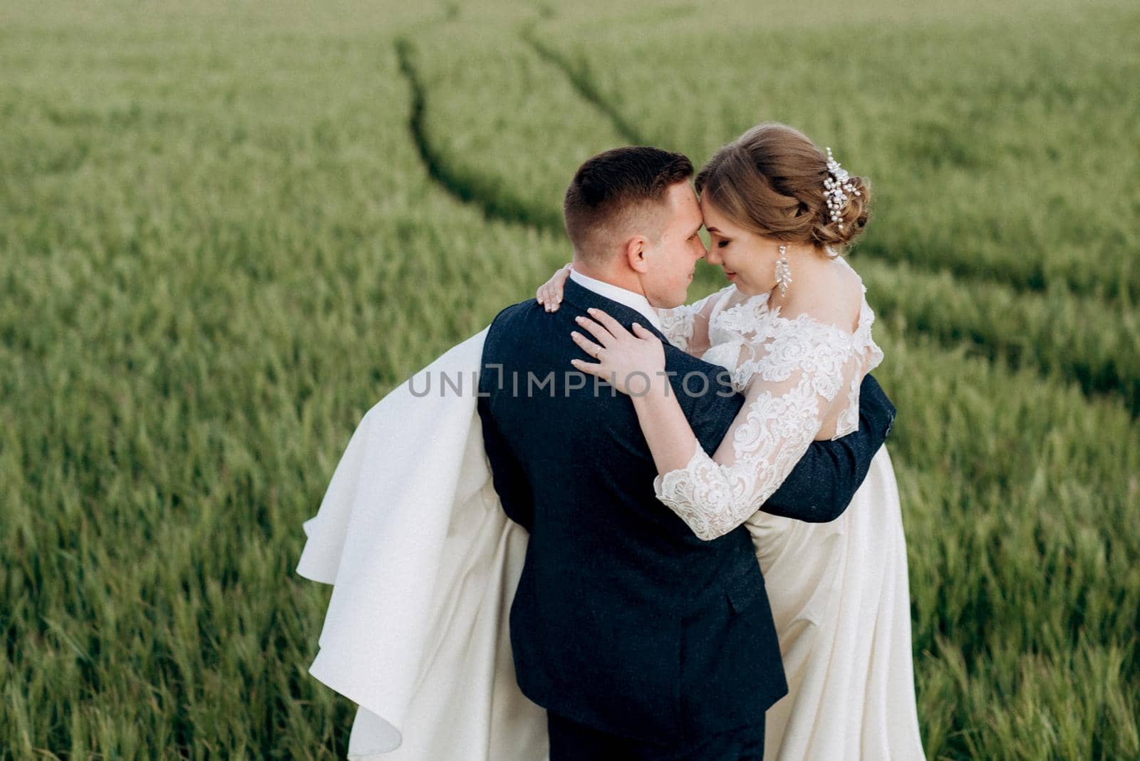 the groom and the bride walk along the wheat green field on a bright day