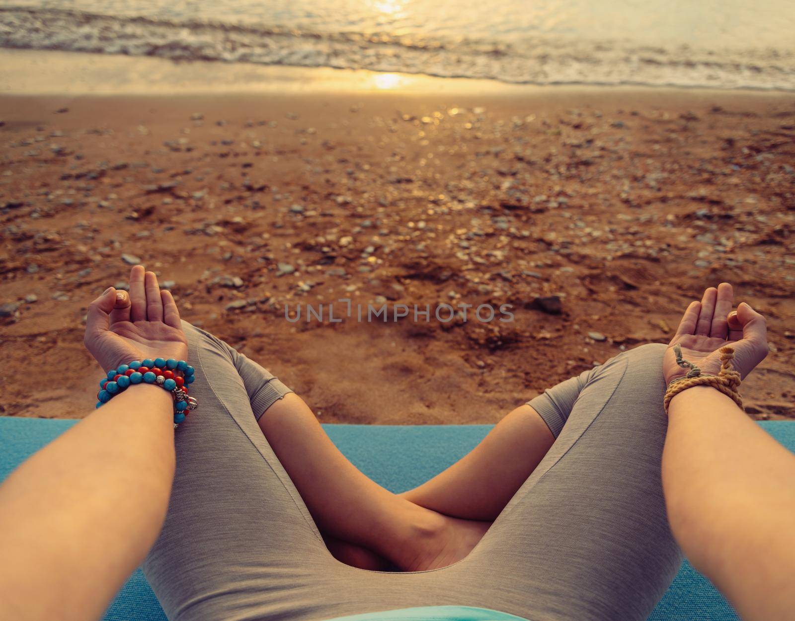 Young woman meditating in pose of lotus on beach at sunset in summer, point of view