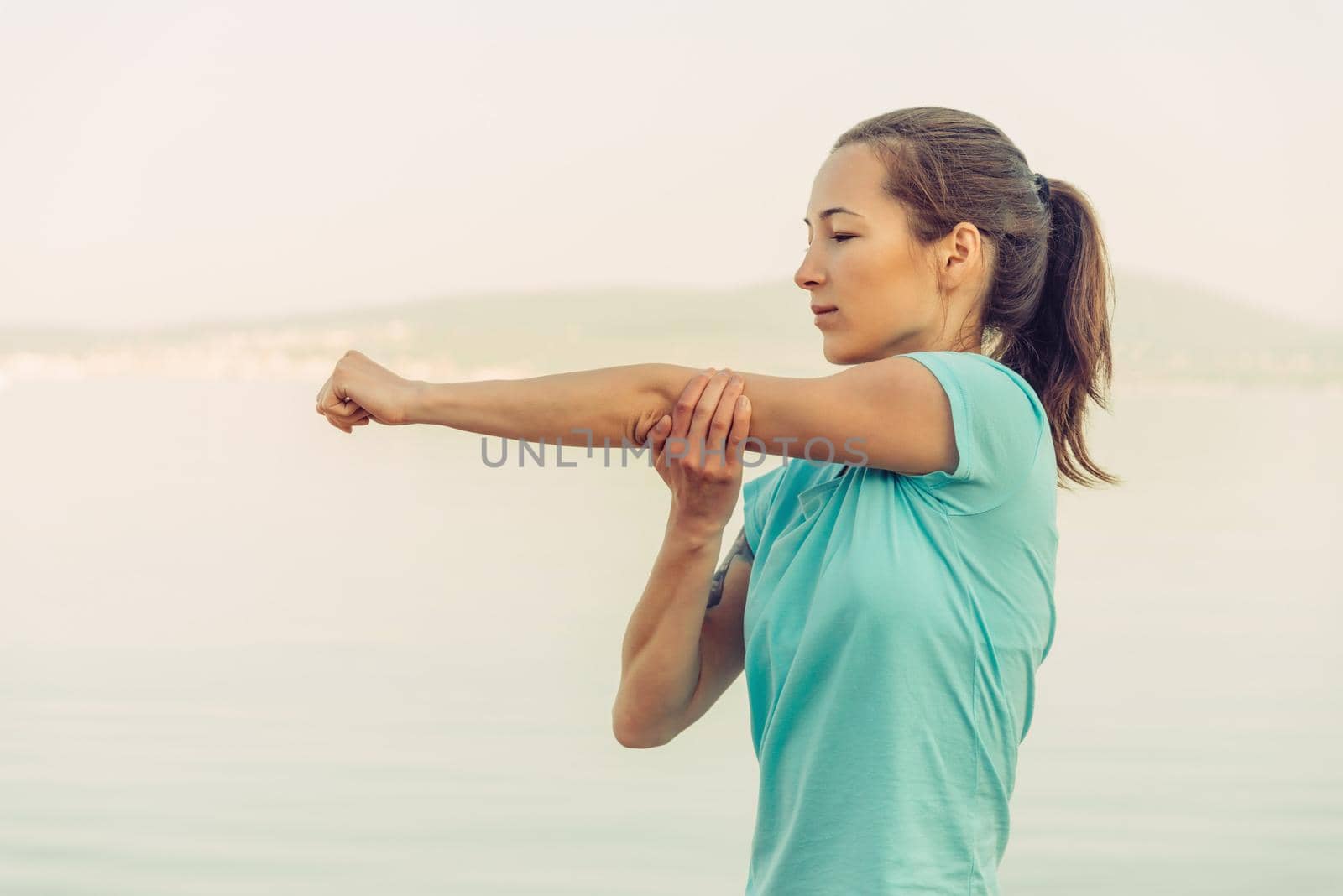 Young woman stretching her arms on beach in summer in the morning. Concept of healthy lifestyle