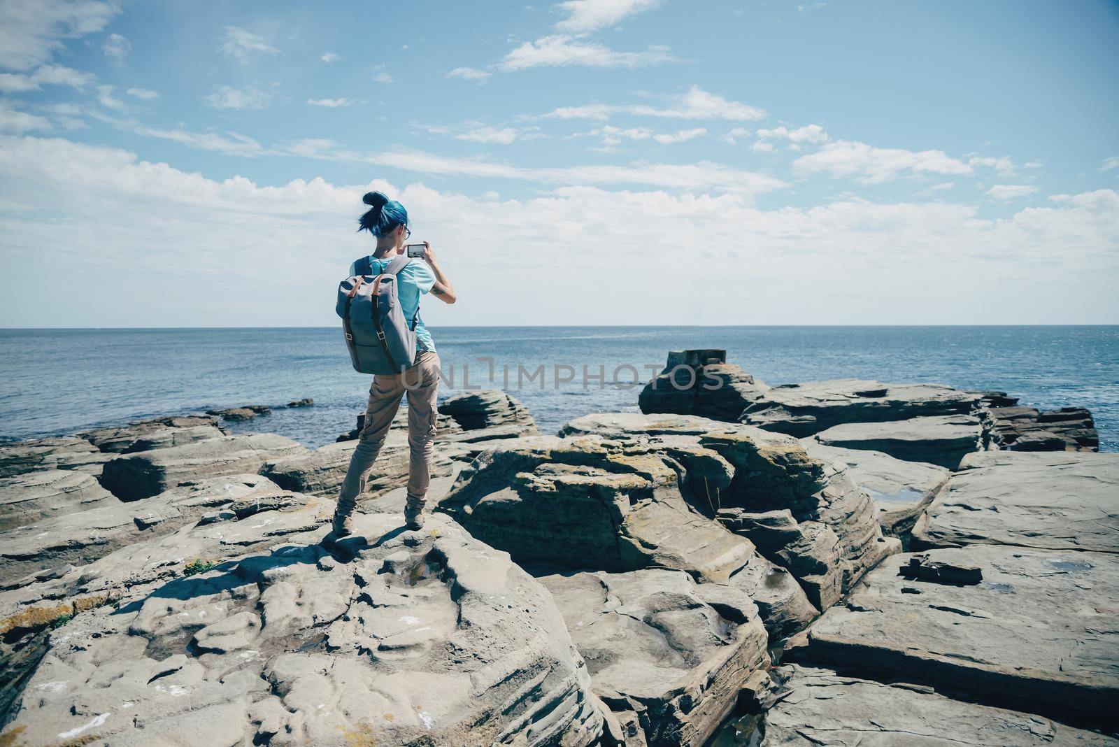 Traveler girl taking photographs beautiful seascape with smartphone on rocky coast in summer