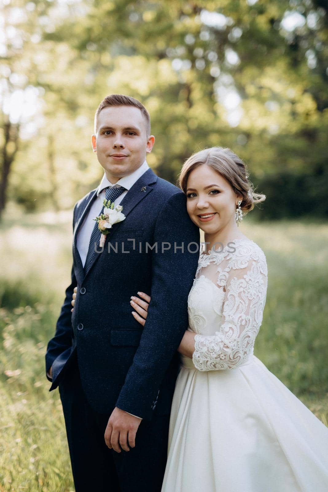 the groom and the bride are walking in the forest near a narrow river on a bright day