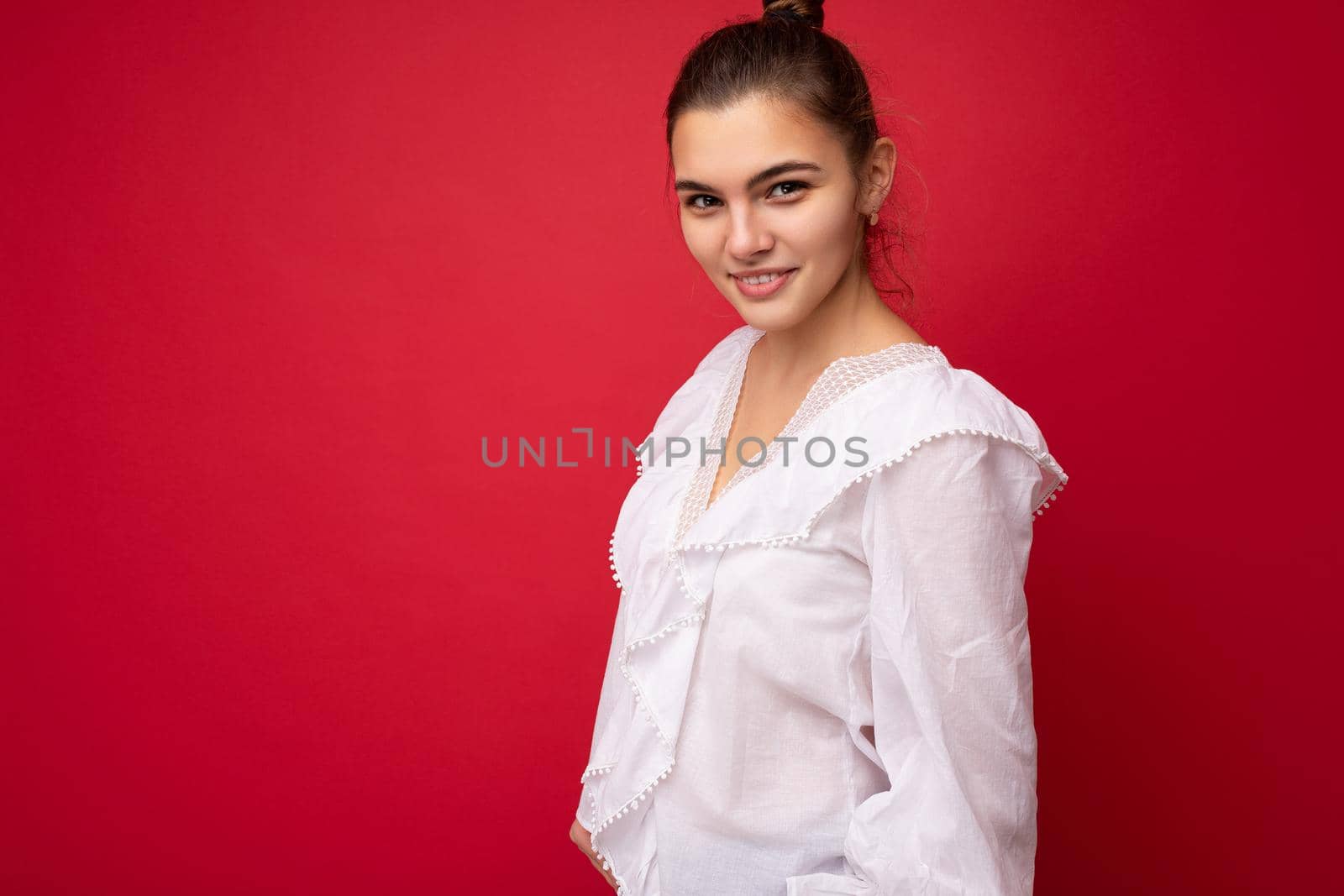 Young beautiful european stylish brunette woman wearing white blouse isolated over red background with positive sincere emotions. Simple and natural looking at the camera. Free space by TRMK