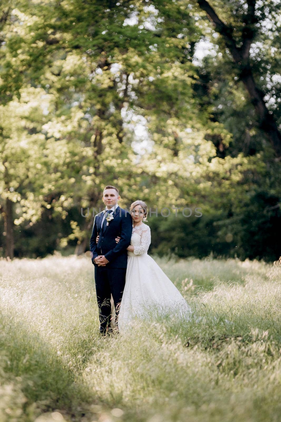 the groom and the bride are walking in the forest near a narrow river on a bright day