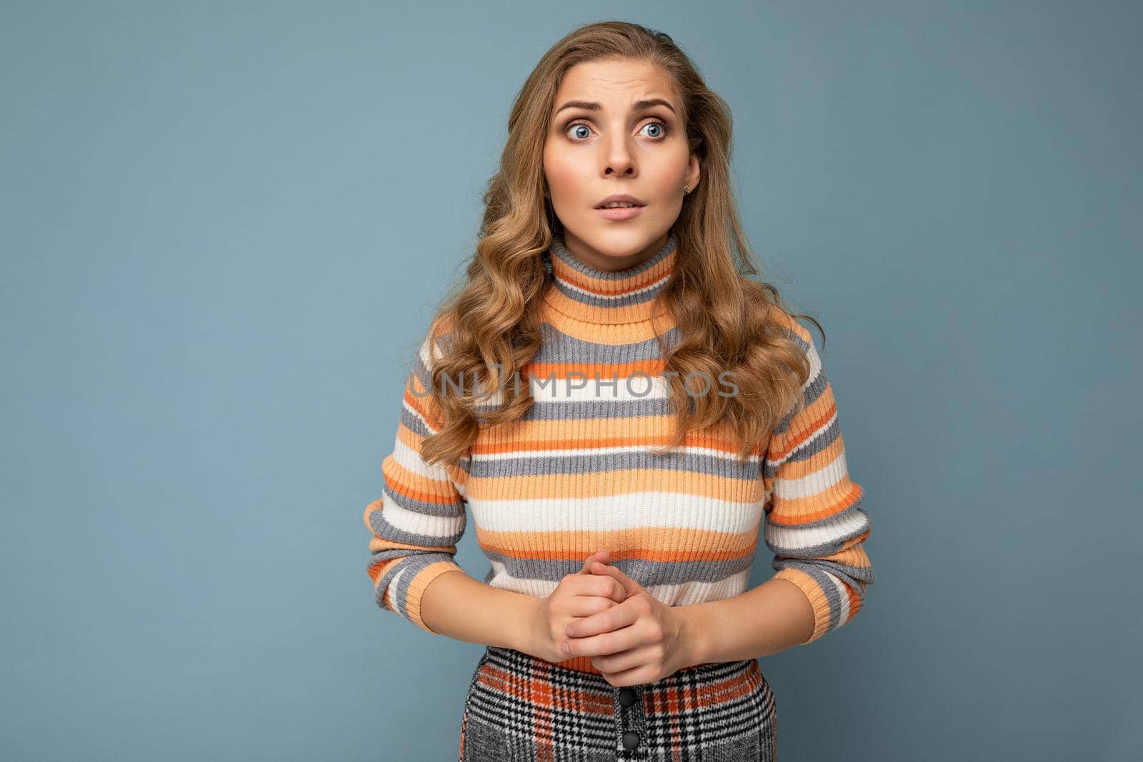 Photo portrait of young attractive beautiful sad upset touchy blonde woman with sincere emotions wearing striped pullover isolated on blue background with copy space by TRMK