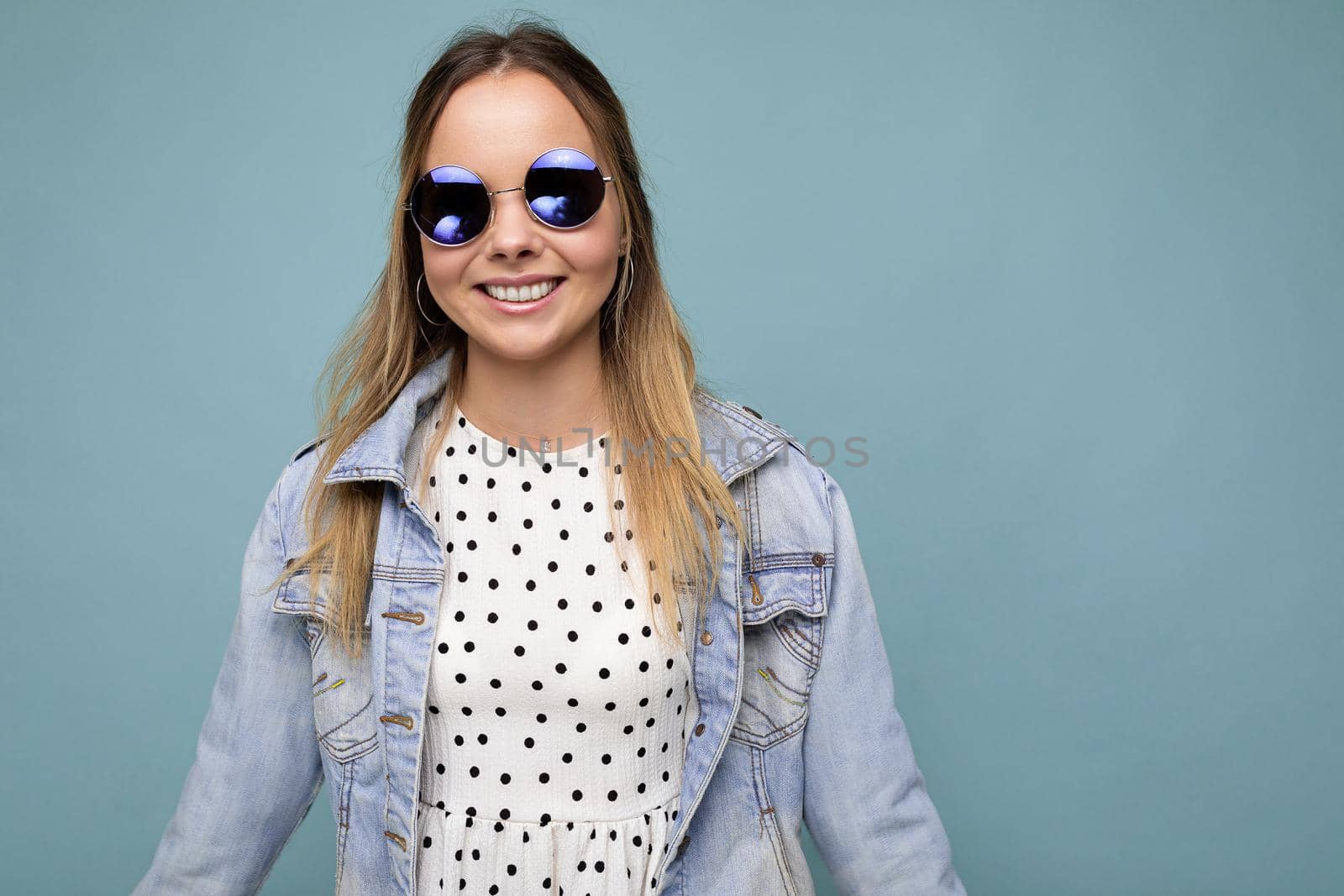 Photo shot of beautiful positive young blonde woman wearing summer casual clothes and stylish sunglasses isolated over colorful background looking at camera.