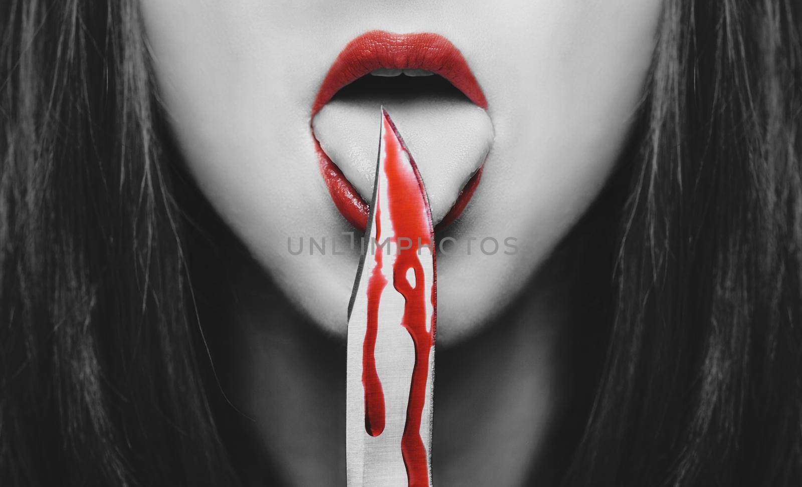 Dangerous young woman licking a knife in blood. Halloween or horror theme. Black and white image with red elements