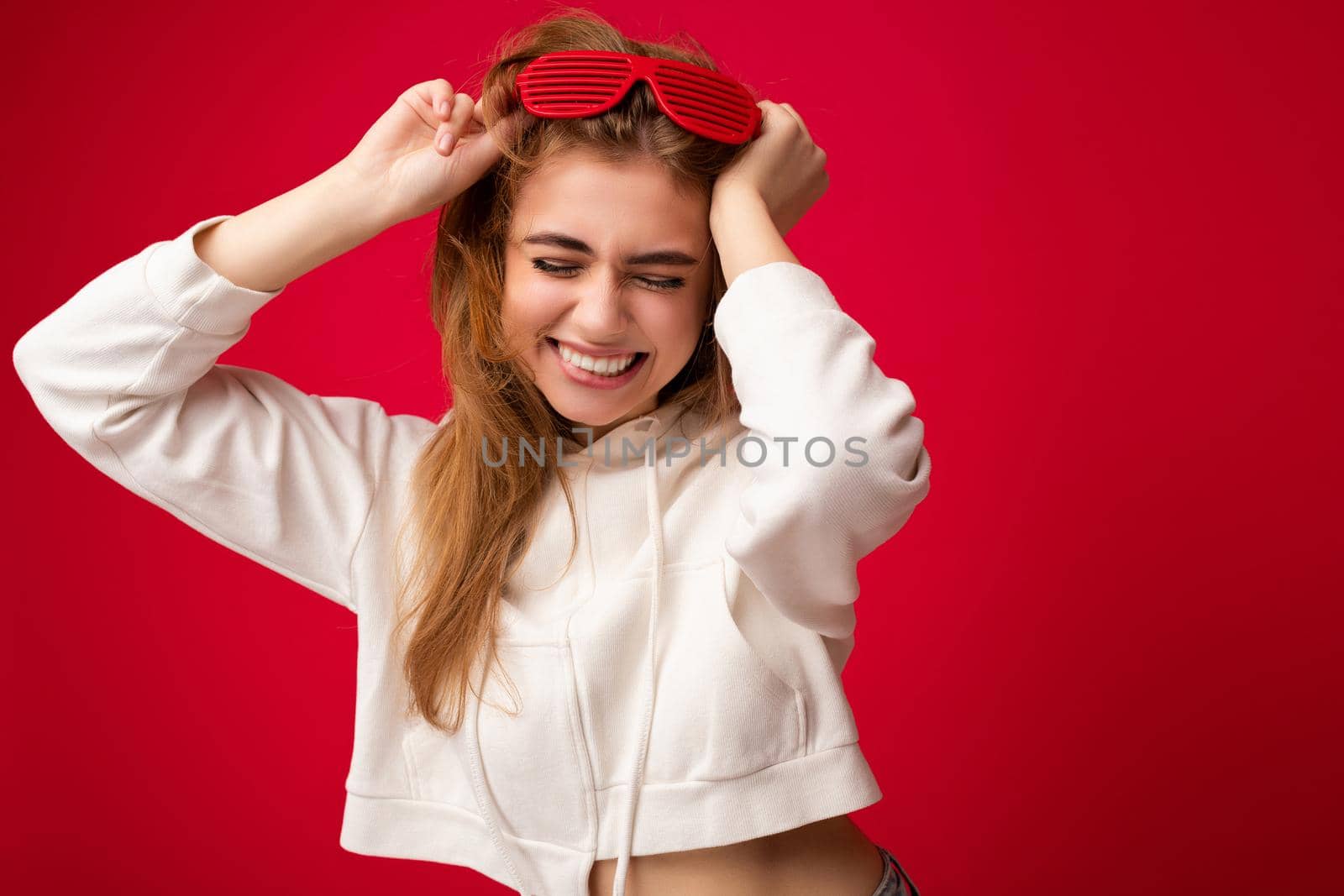 Photo shot of beautiful positive young blonde woman wearing casual clothes and stylish optical glasses isolated over colorful background wall and having fun.
