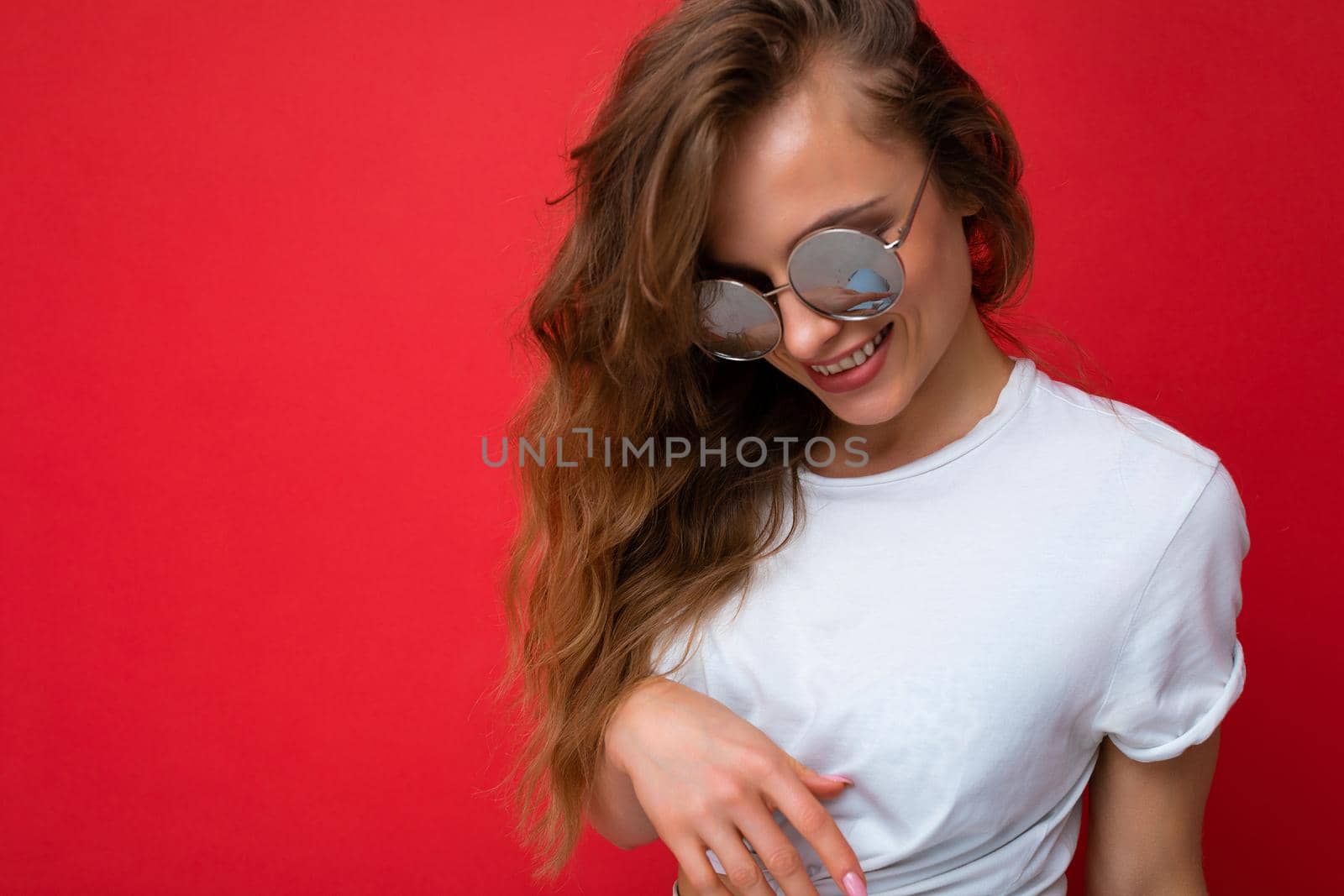 Attractive happy smiling young blonde woman wearing everyday stylish clothes and modern sunglasses isolated on colorful background wall looking down.