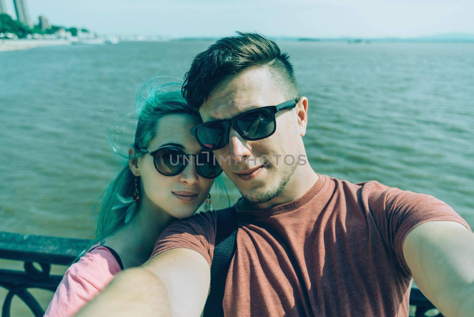 Traveler young loving couple doing self-portrait on background of sea in summer. Girl with blue hair