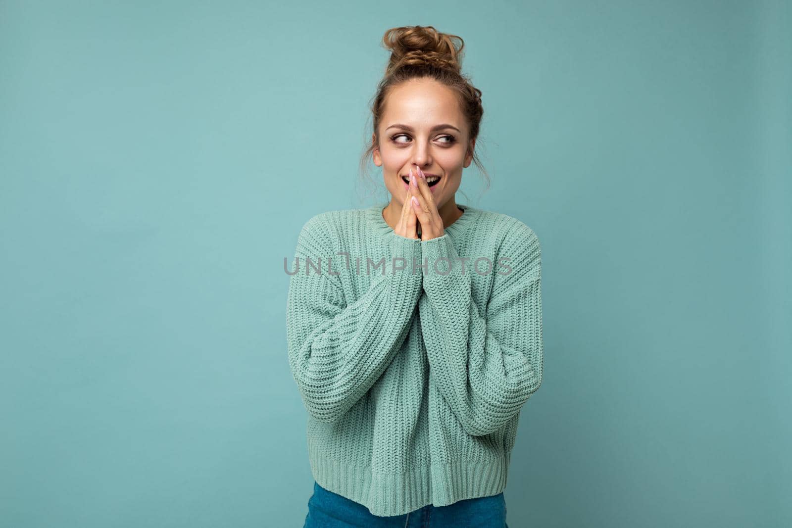 Portrait of young happy positive satisfied attractive beautiful blonde woman with sincere emotions wearing casual blue pullover isolated on blue background with copy space.