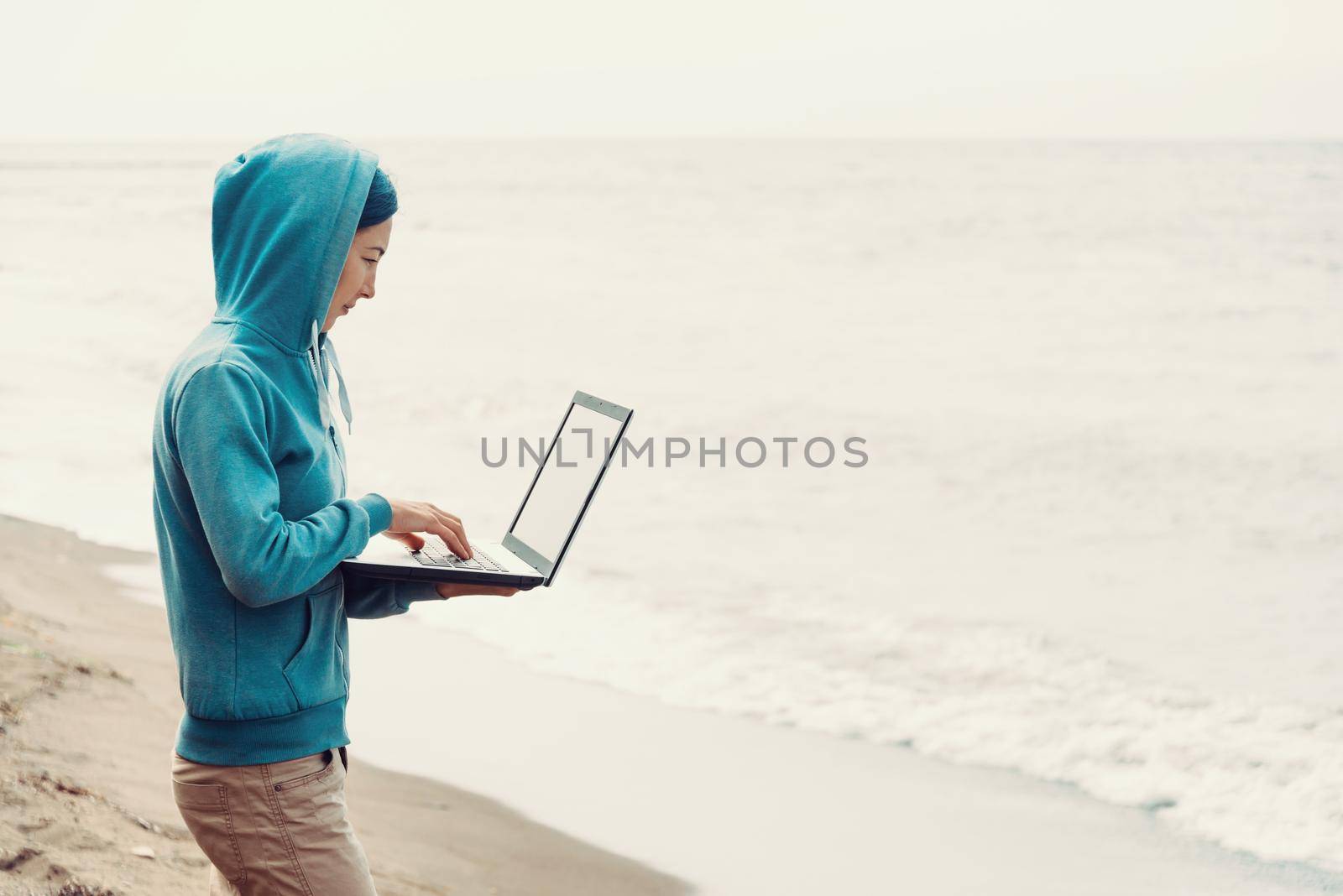 Freelancer girl standing on beach near the sea and working on laptop. Freelance concept