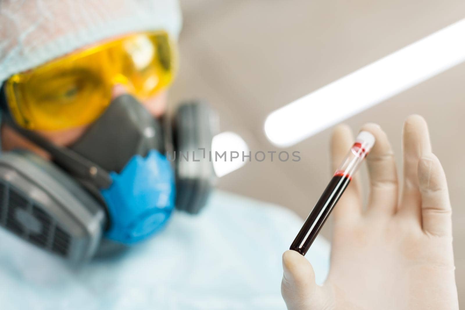 Researcher in protective wear is carefully looking at a blood sample in a test tube. Creating a vaccine. Close up photo. Focus on test tube.