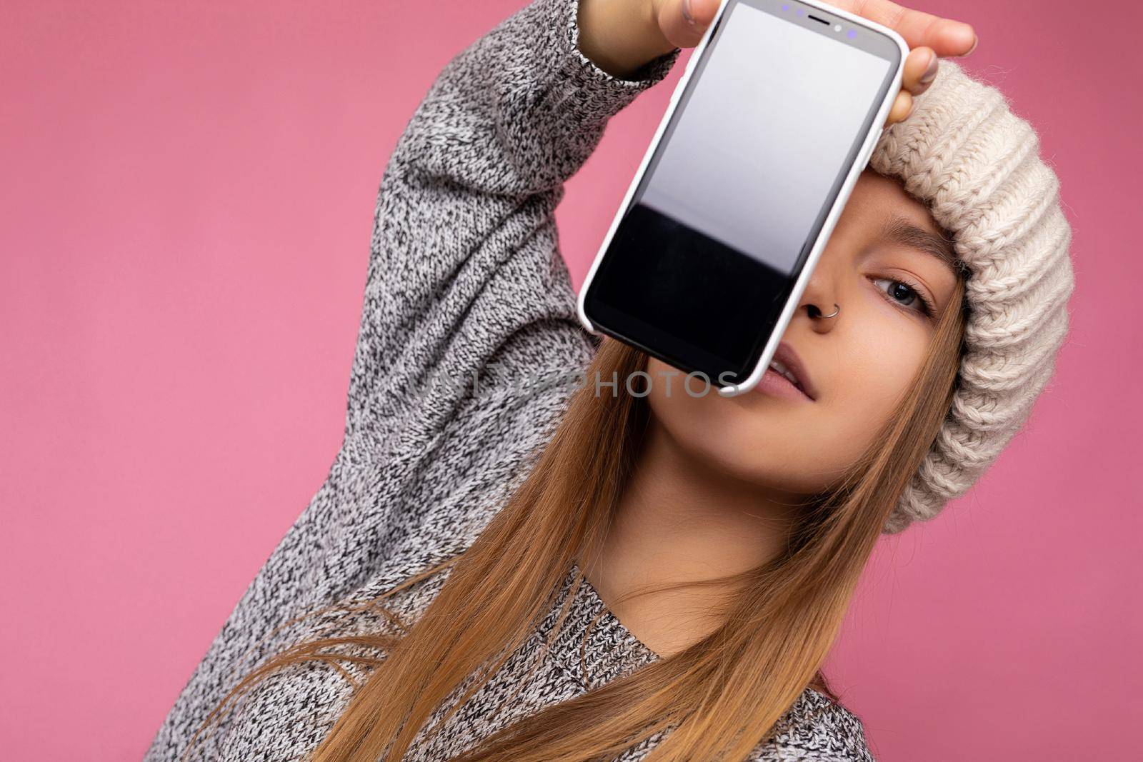 Photo of beautiful sexy young woman good looking wearing casual stylish outfit standing isolated on background with copy space holding smartphone showing phone in hand with empty screen display for mockup looking at camera.