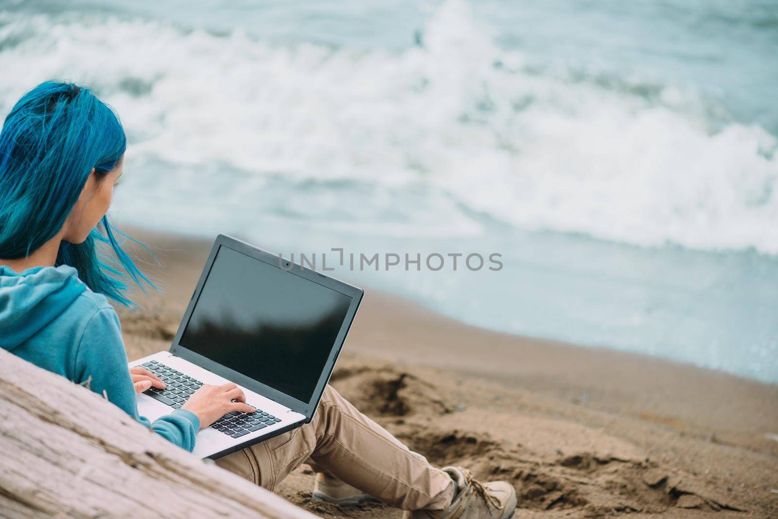 Freelancer young woman with blue hair working on laptop on beach near the sea. Freelance concept. Focus on hand
