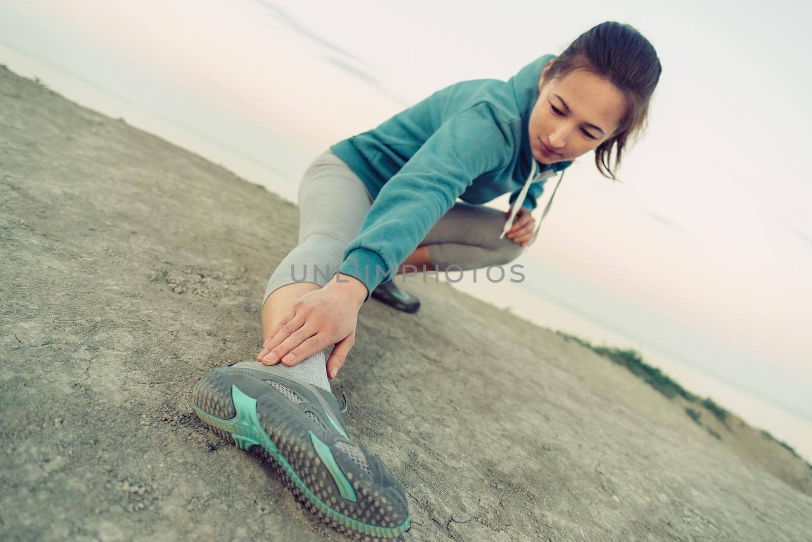 Girl stretching her legs and preparing to run on coast in summer. Concept of healthy lifestyle