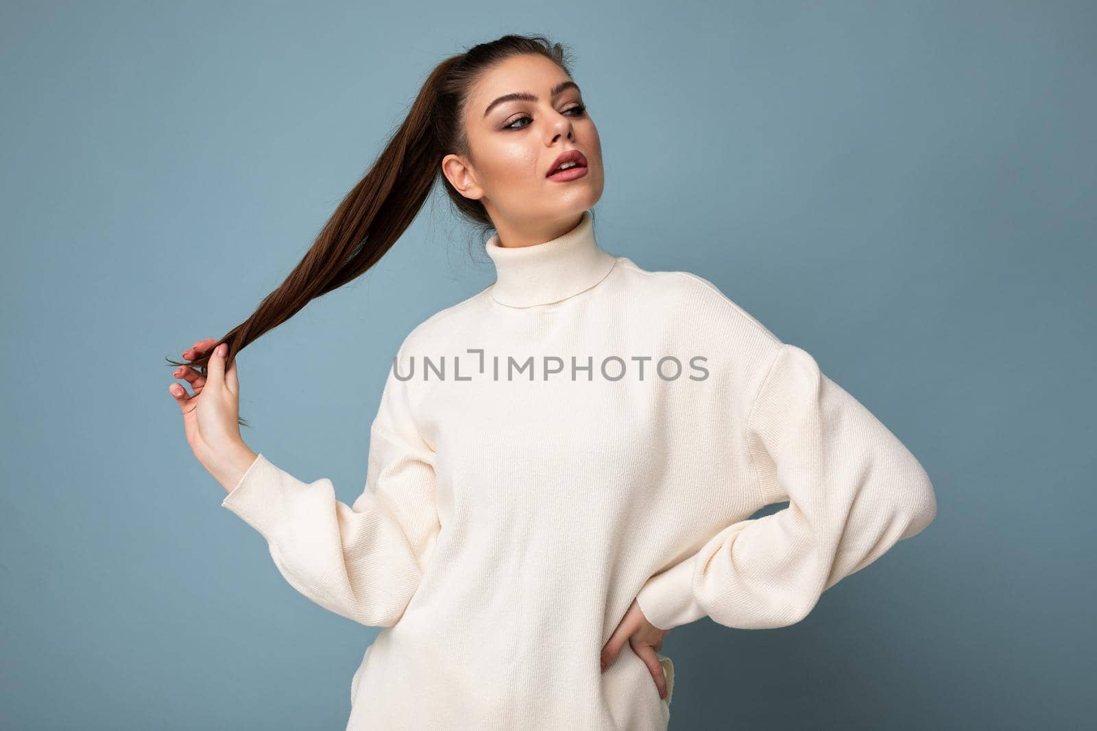 Young fascinating sexy caucasian fashion brunette woman wearing casual white sweater poising isolated on blue background wall.