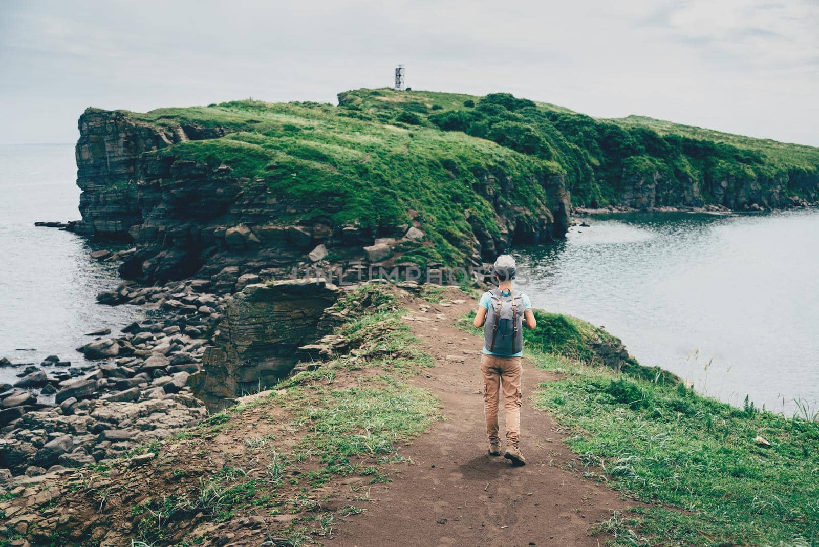 Tourist young woman with backpack walking on island in the sea in summer, rear view