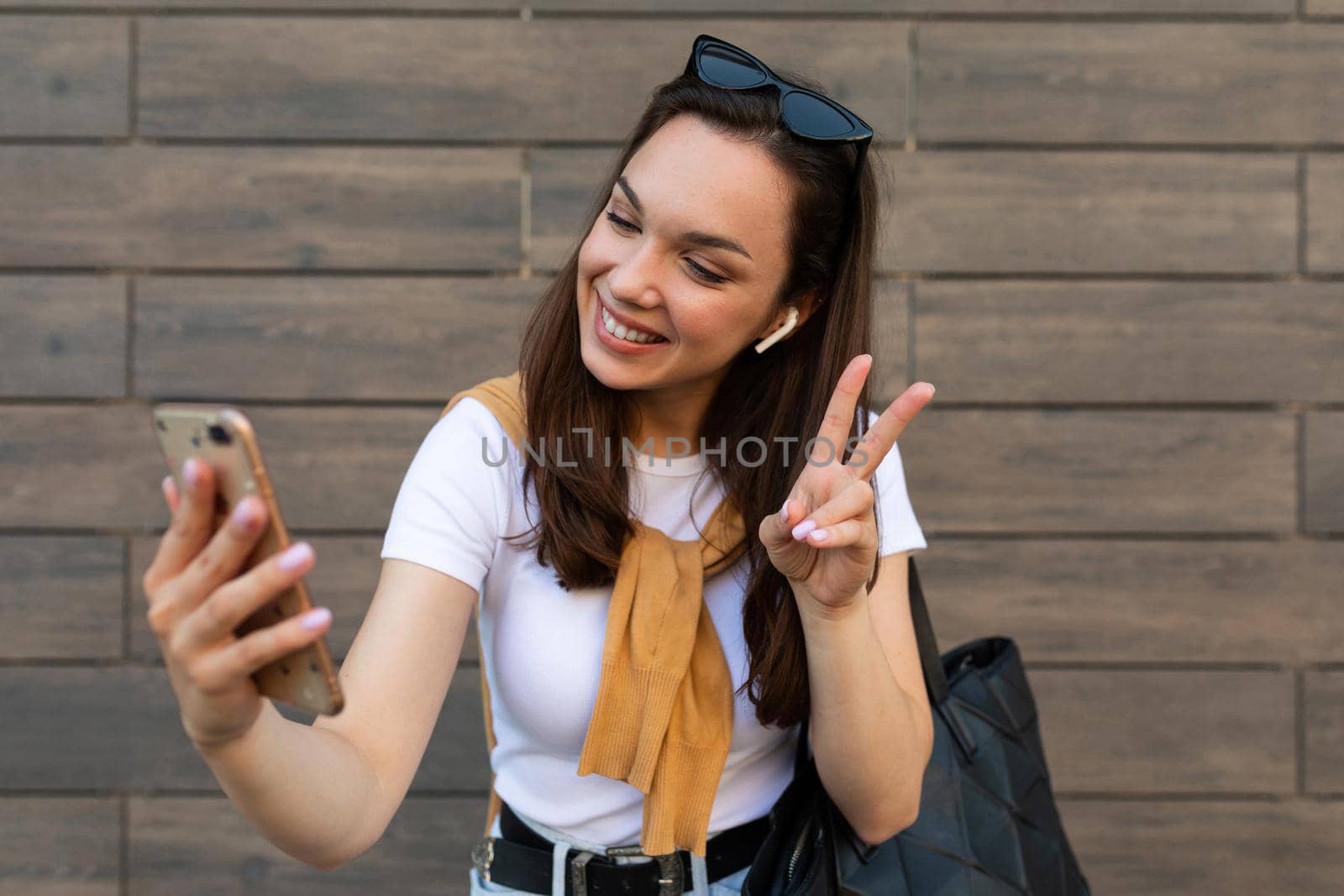 Surprised young woman posing isolated on brown background, studio portrait. People lifestyle concept. Mock up copy space. Using mobile phone, typing sms message.