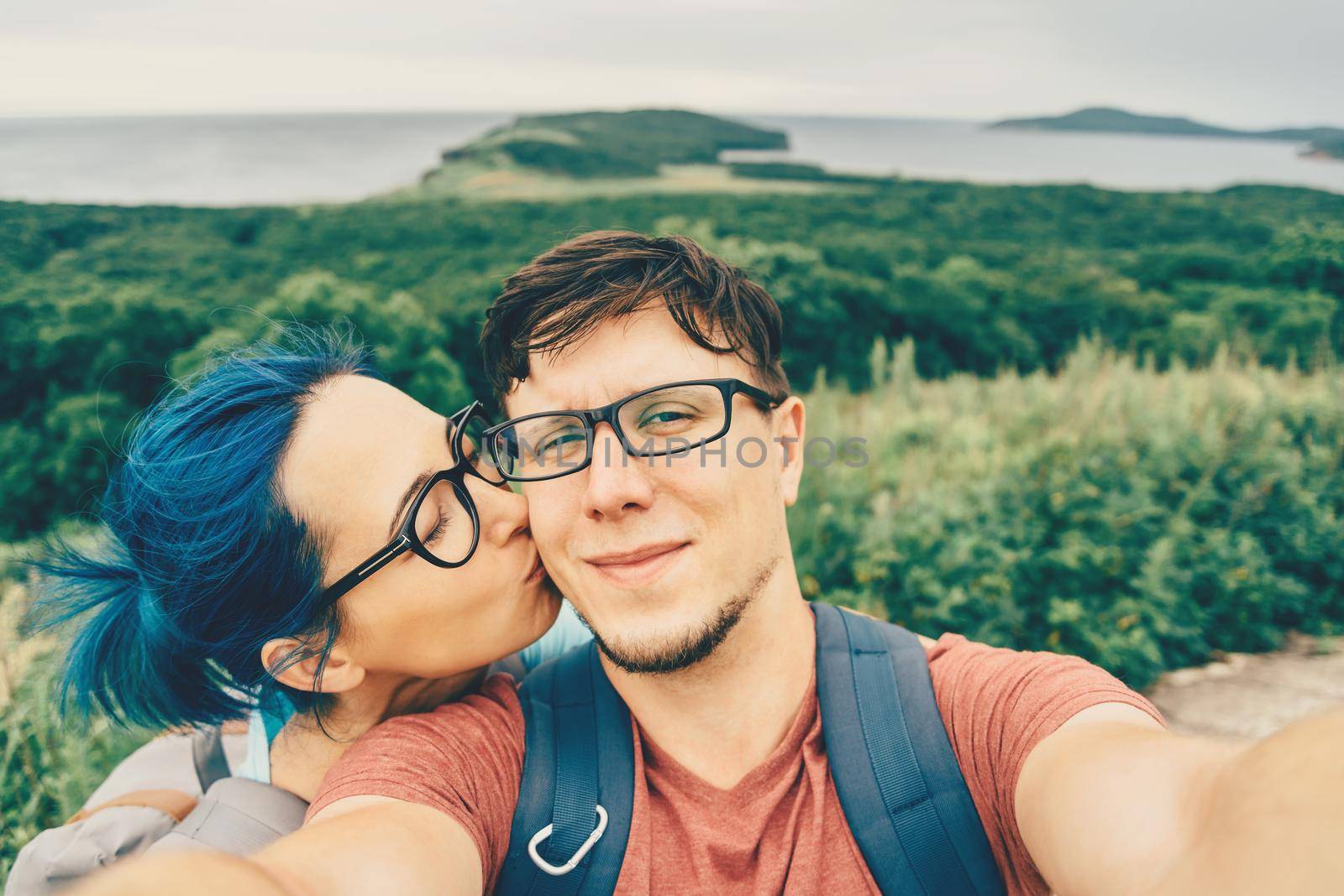 Traveler young loving couple doing selfie on nature in summer. Woman kissing a man