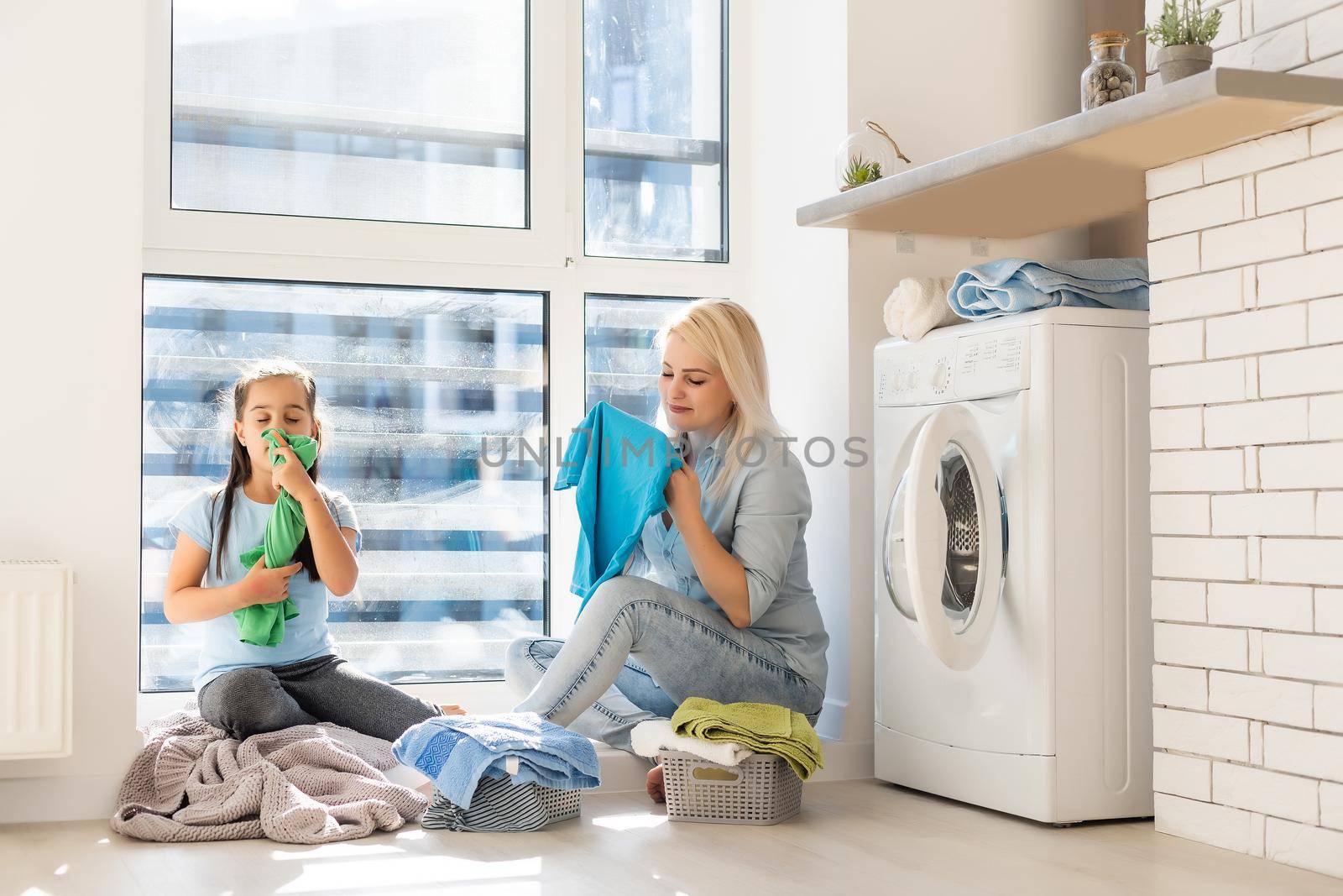 Happy housewife and her daughter with linen near washing machine