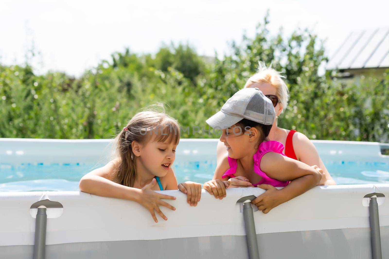 Mother and two daughters playing in pool water.Woman and two girls have fun in home pool splashing water and smiling