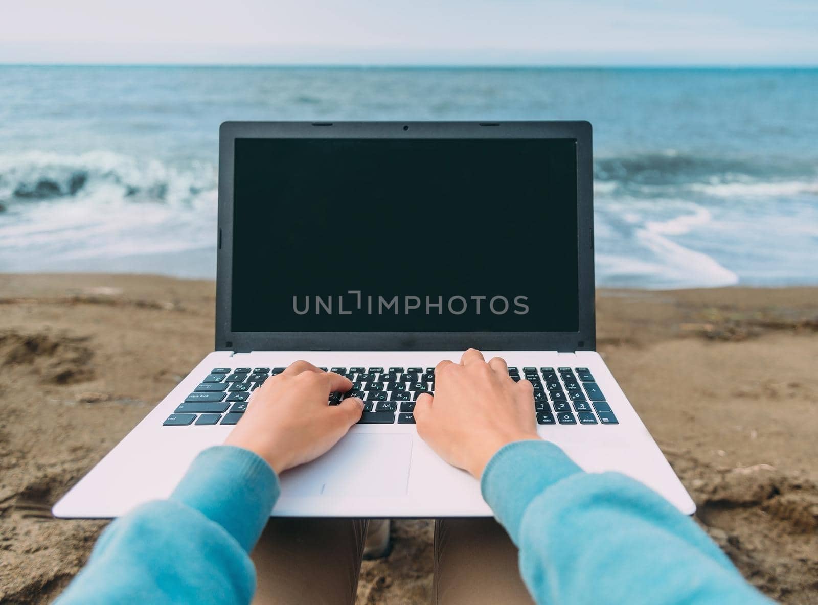 Freelancer woman working on laptop on beach on background of sea. Space for text on laptop. Point of view shot