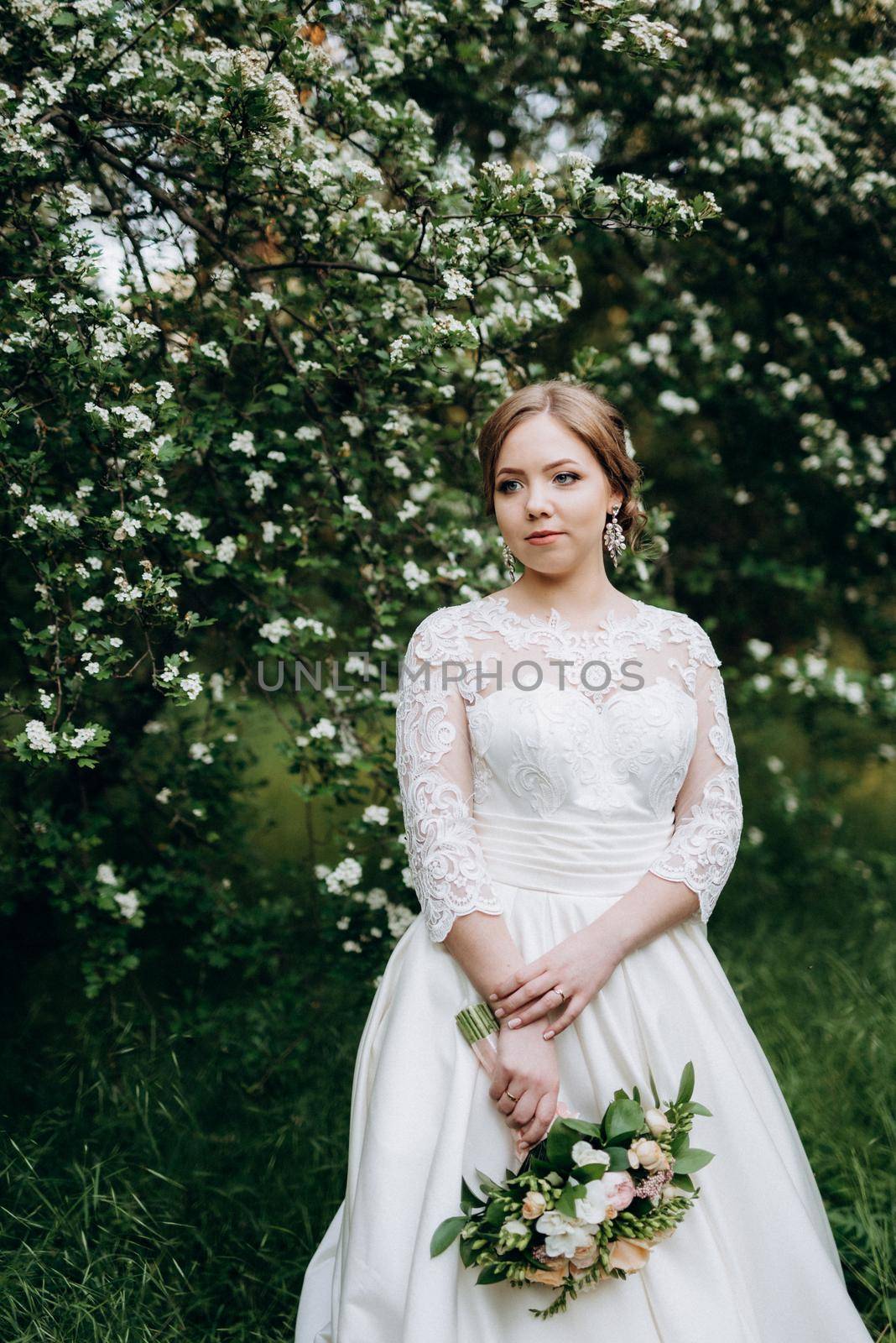 bride with a wedding bouquet in the forest near the bushes blooming with white flowers