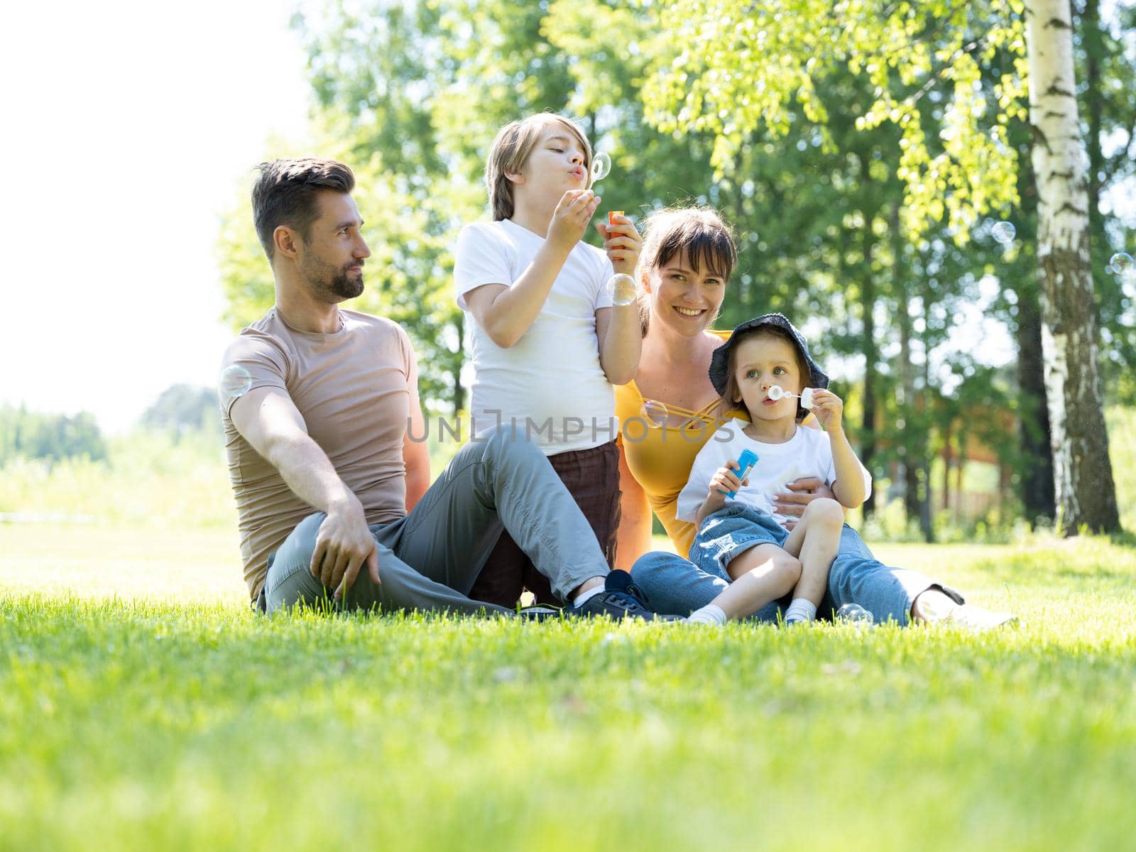 Happy family of mother, father and two children blowing bubbles in summer park