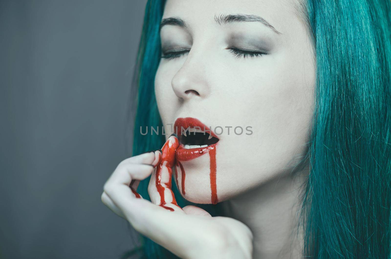 Beautiful vampire young woman wipes the blood from her lips. Halloween or horror theme