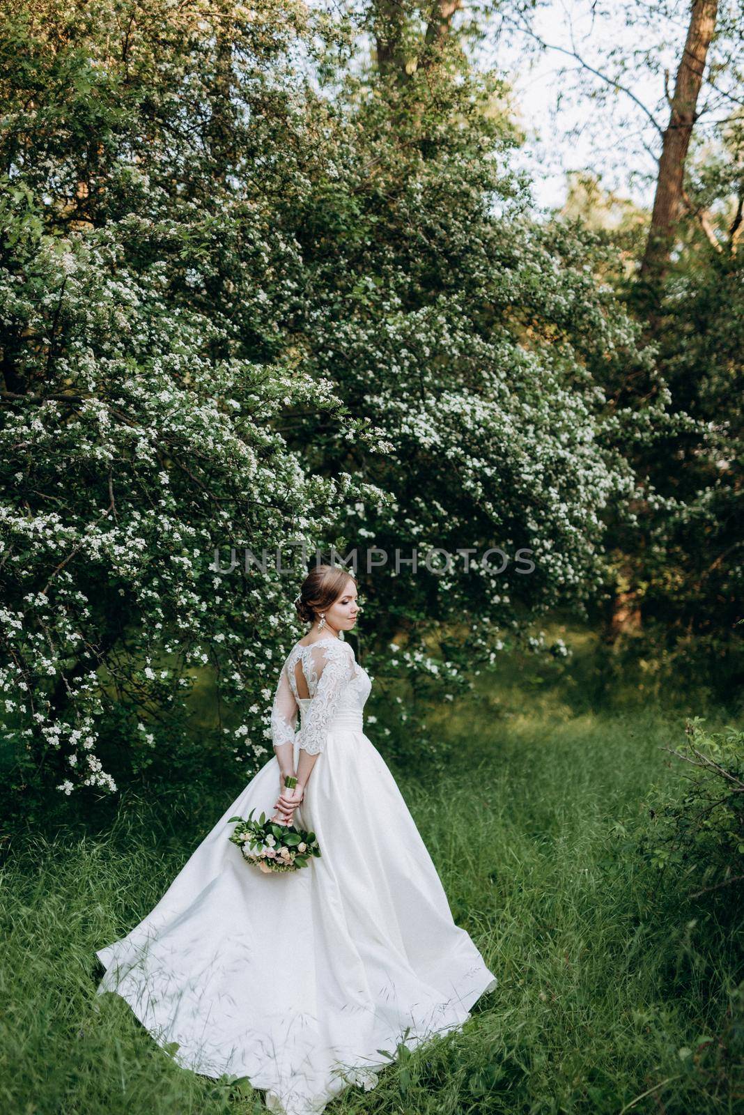 bride with a wedding bouquet in the forest near the bushes blooming with white flowers