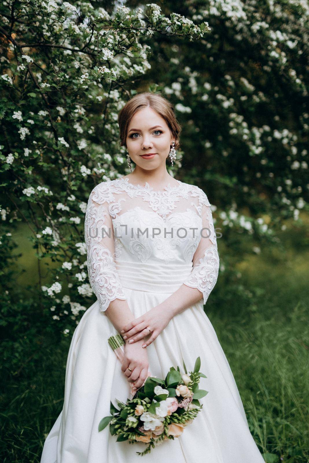 bride with a wedding bouquet in the forest near the bushes blooming with white flowers