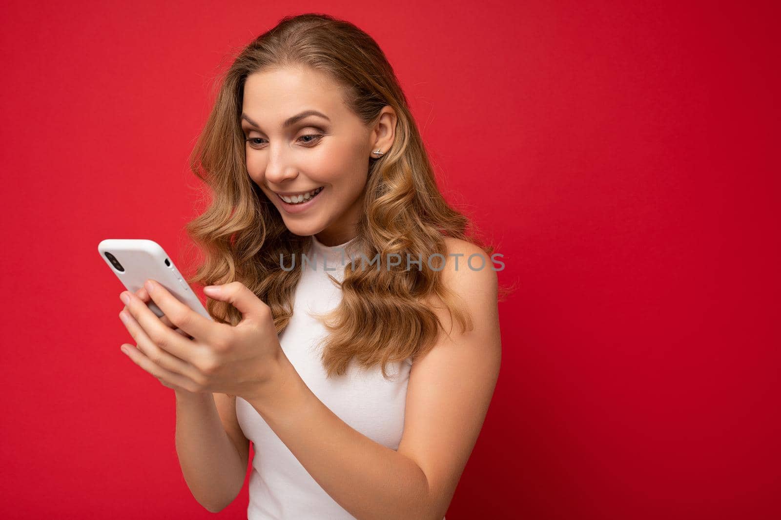 side-profile Photo shot of attractive positive good looking young woman wearing casual stylish outfit poising isolated on background with empty space holding in hand and using mobile phone messaging sms looking at smartphone display screen.