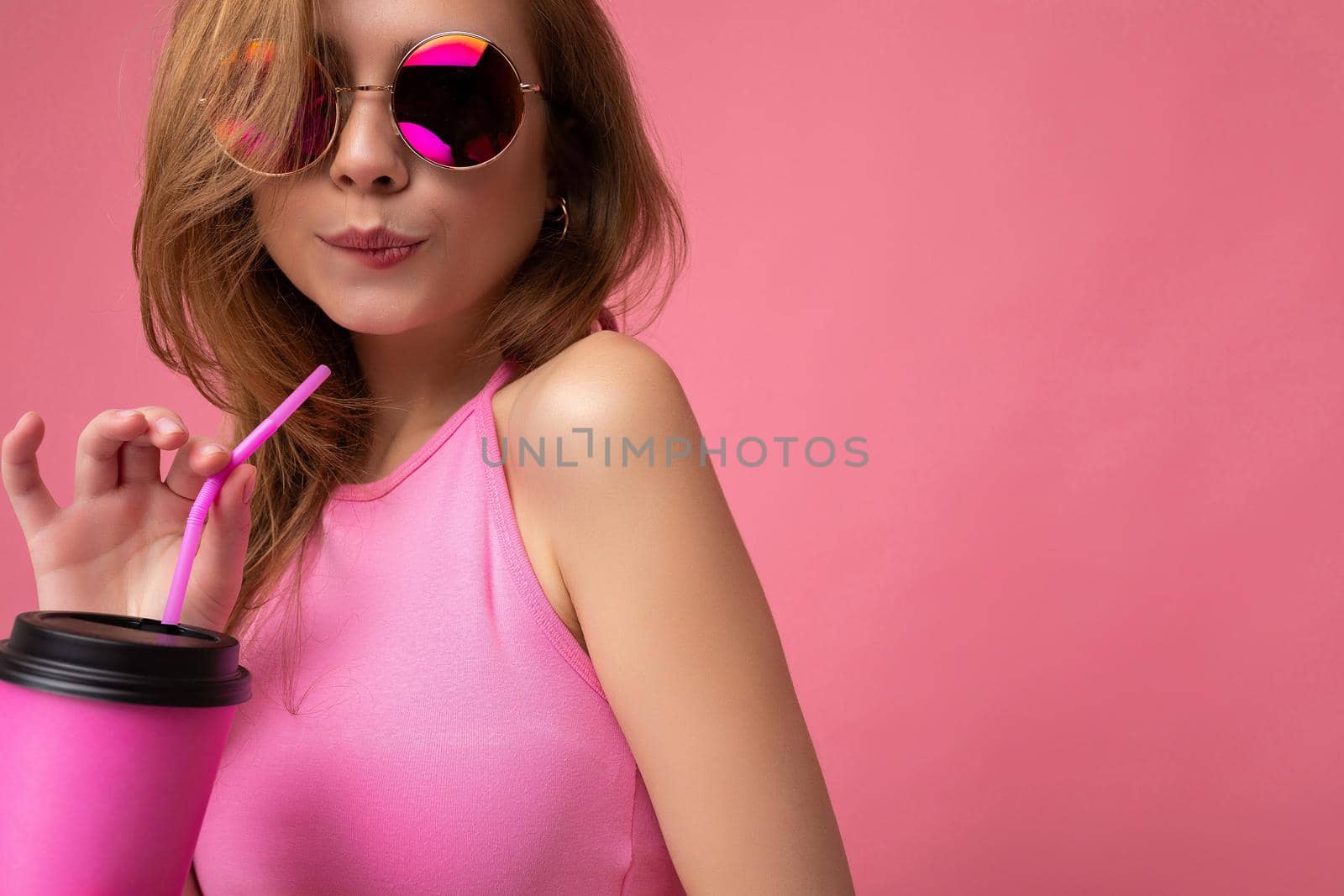 Closeup portrait of sexy pretty young happy blonde woman wearing pink top and colourful sunglasses isolated over pink background holding coffee paper cup for cutout drinking and flirting. copy space